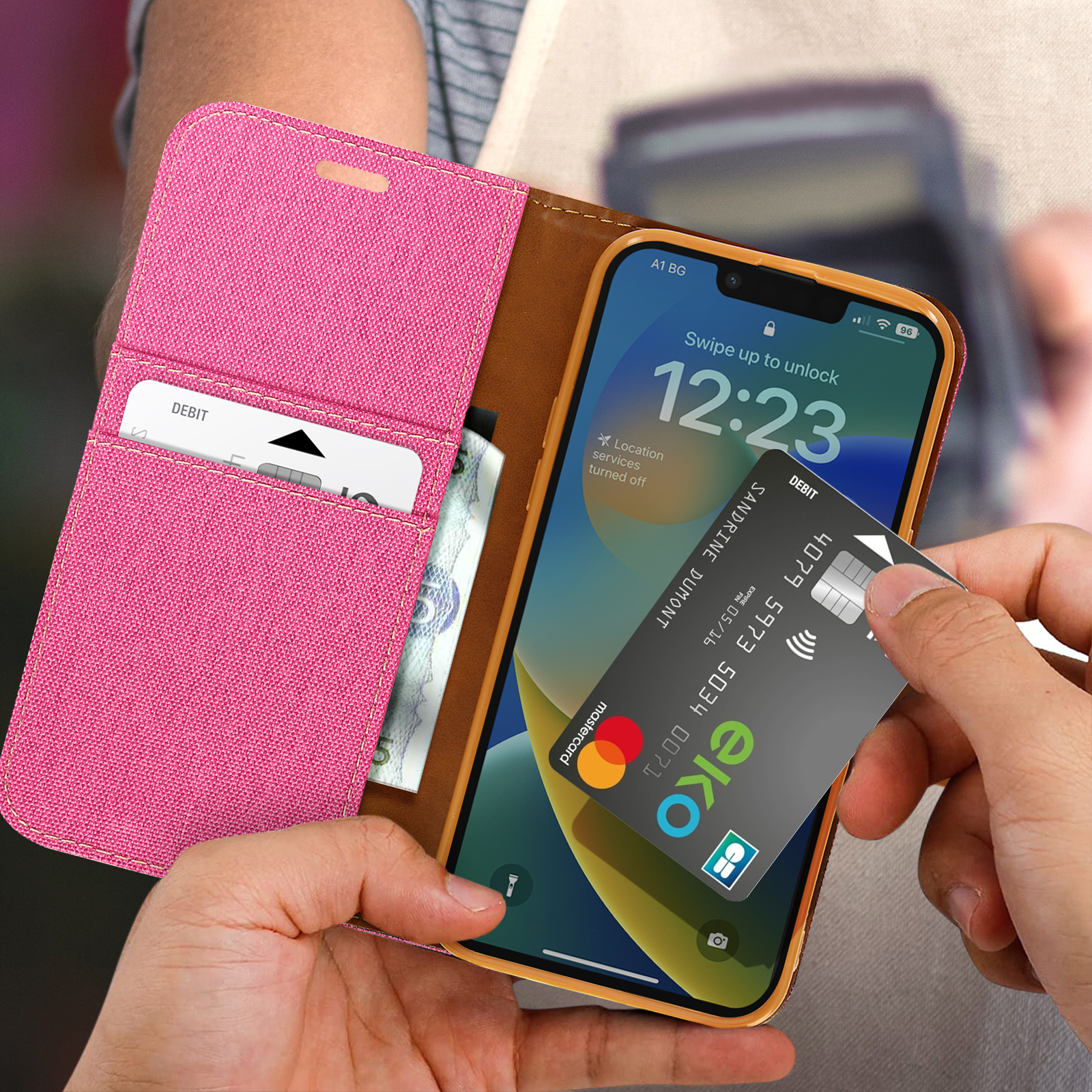 Telefono in custodia rosa con carte, carta di debito in mano, su sfondo in pelle marrone.