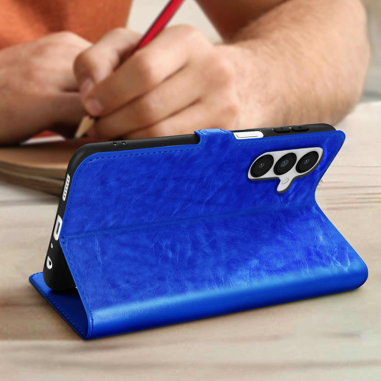 Custodia blu per telefono con supporto, telefono all'interno. Persona che scrive sullo sfondo.