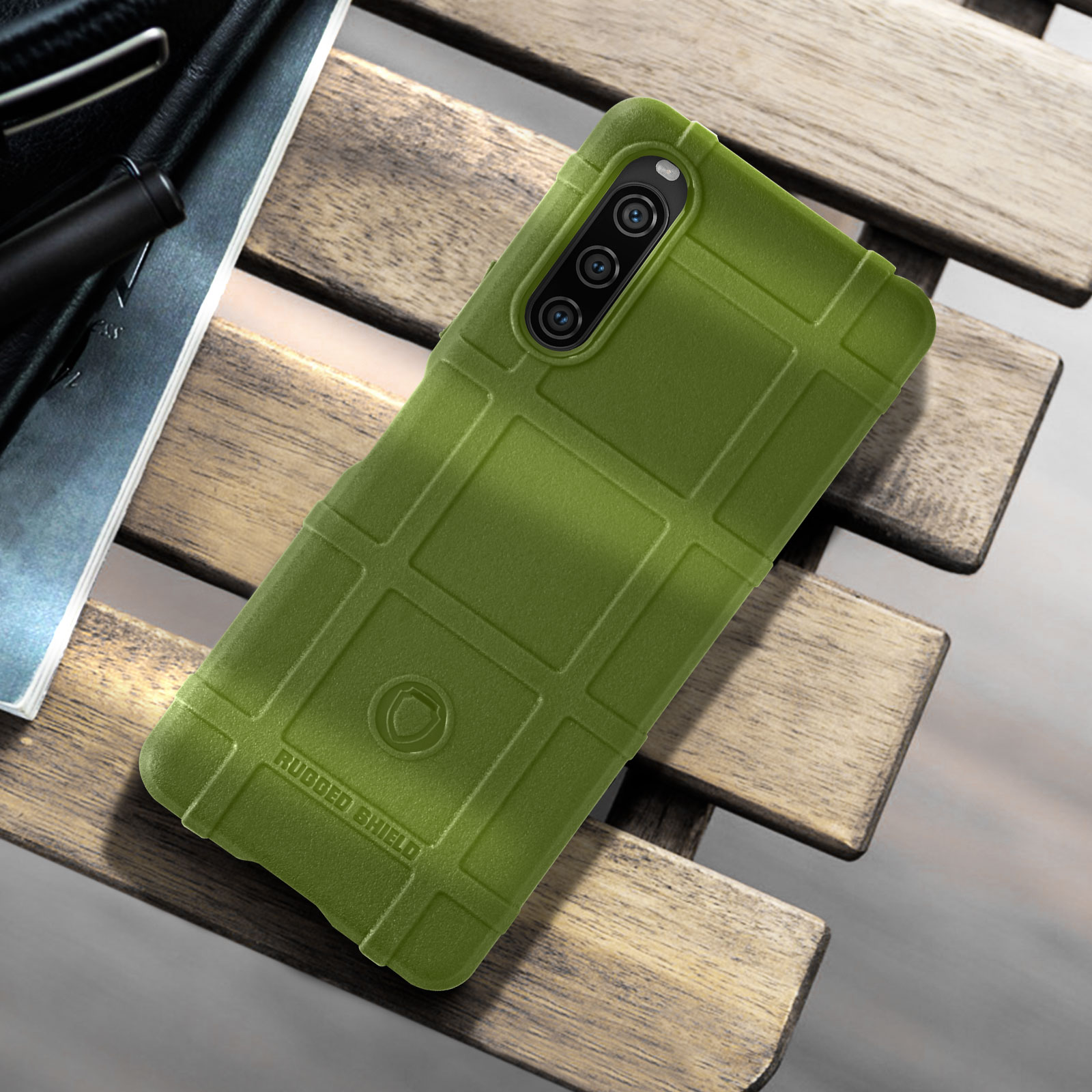 Una custodia per telefono verde oliva su un tavolo di legno. Ha un motivo strutturato, simile a una griglia, e ritagli per la fotocamera.