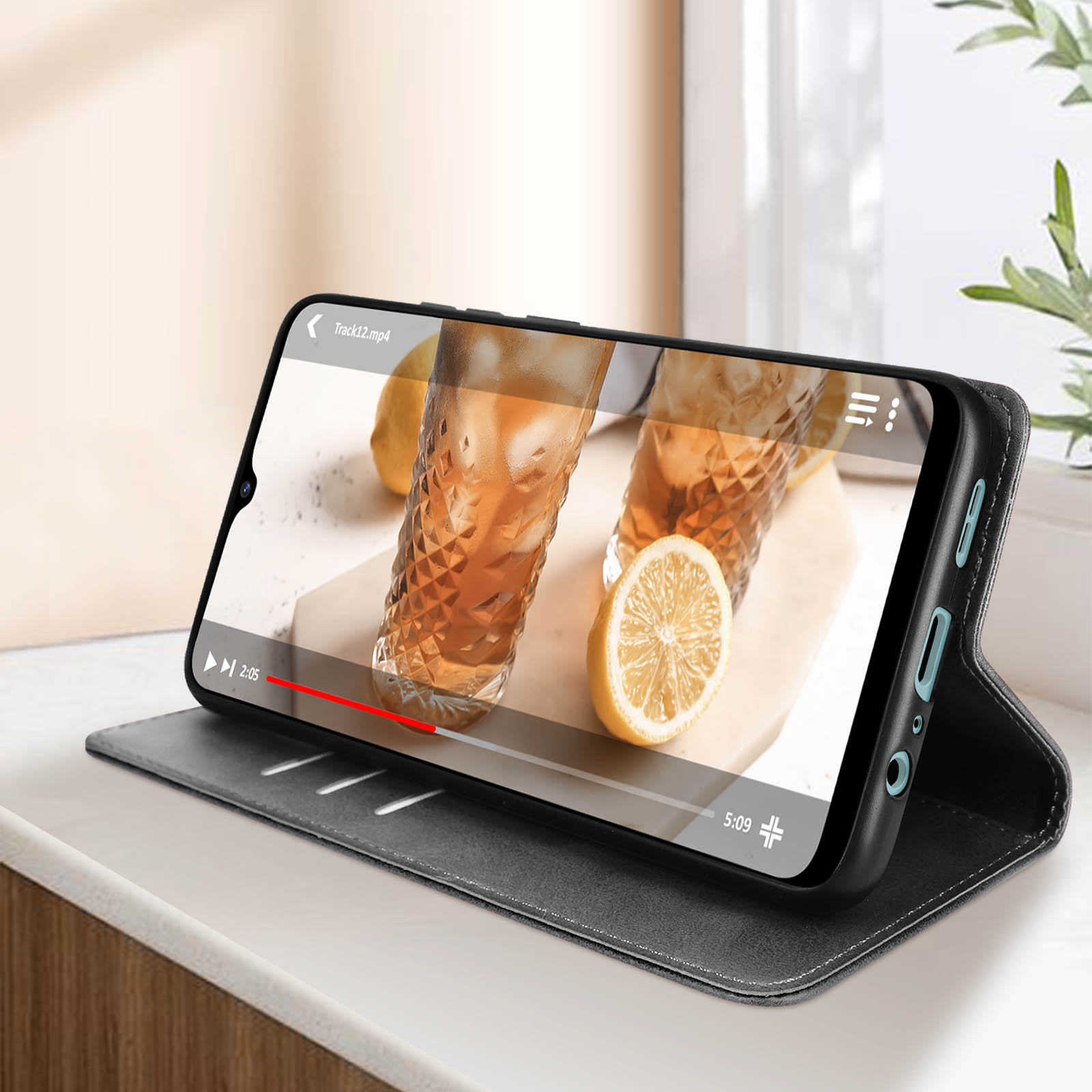 Telefono in custodia nera che mostra un video, appoggiato su un tavolo. Limone e bicchieri sullo sfondo.