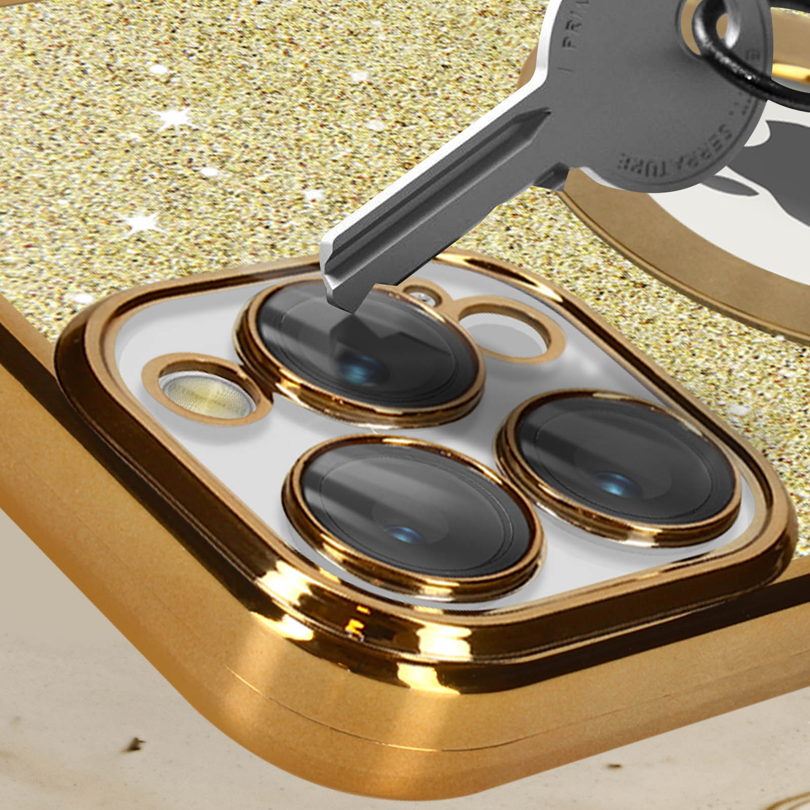 Una chiave inserita in una custodia dorata per telefono con lenti nere e sfondo glitterato.
