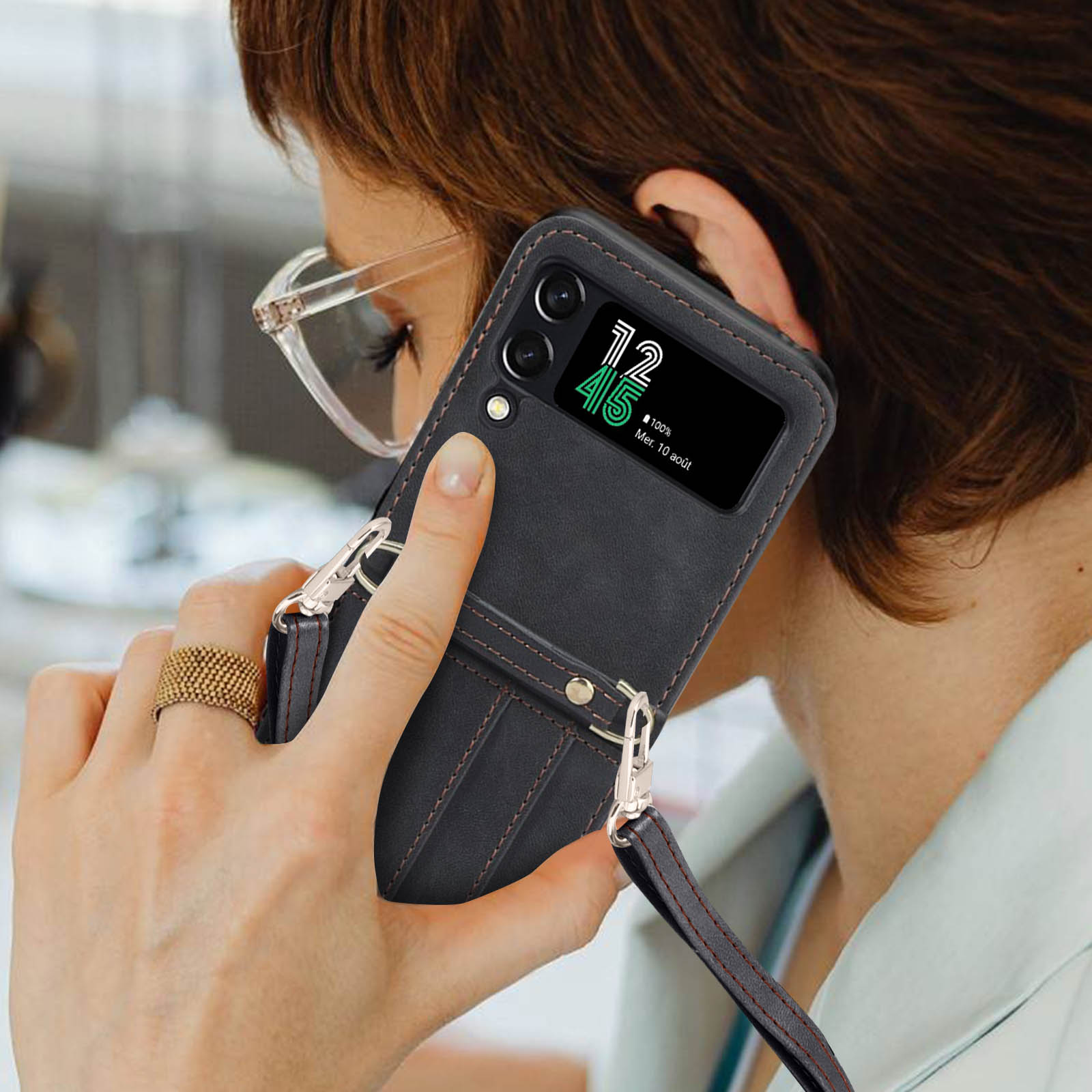 Donna che tiene in mano un telefono nero con custodia, indossa occhiali e un anello. Schermo del telefono visibile.