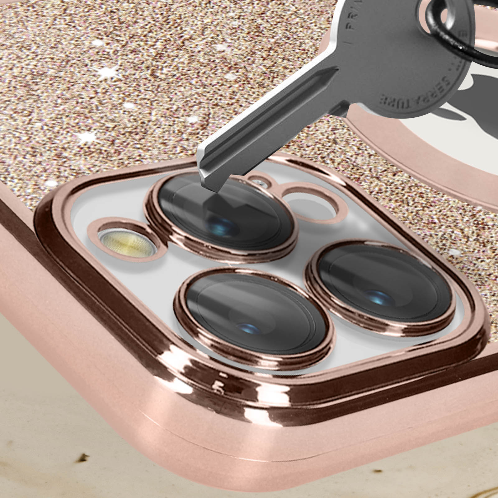 Funda de teléfono oro rosa con llave apuntando a lentes de cámara, fondo brillante.