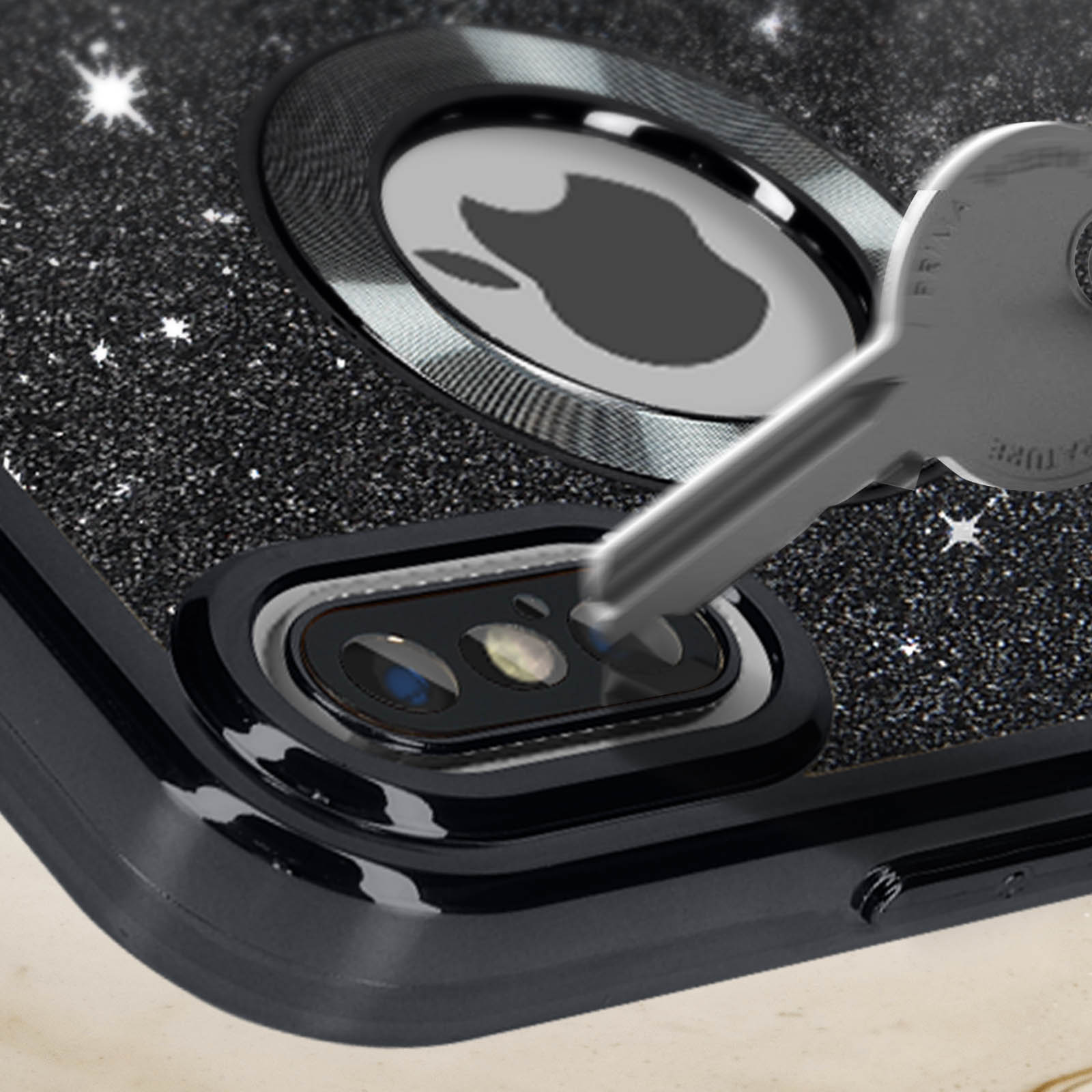 Primo piano di una custodia per telefono con chiave. La custodia ha glitter e logo Apple. La chiave tocca la fotocamera.