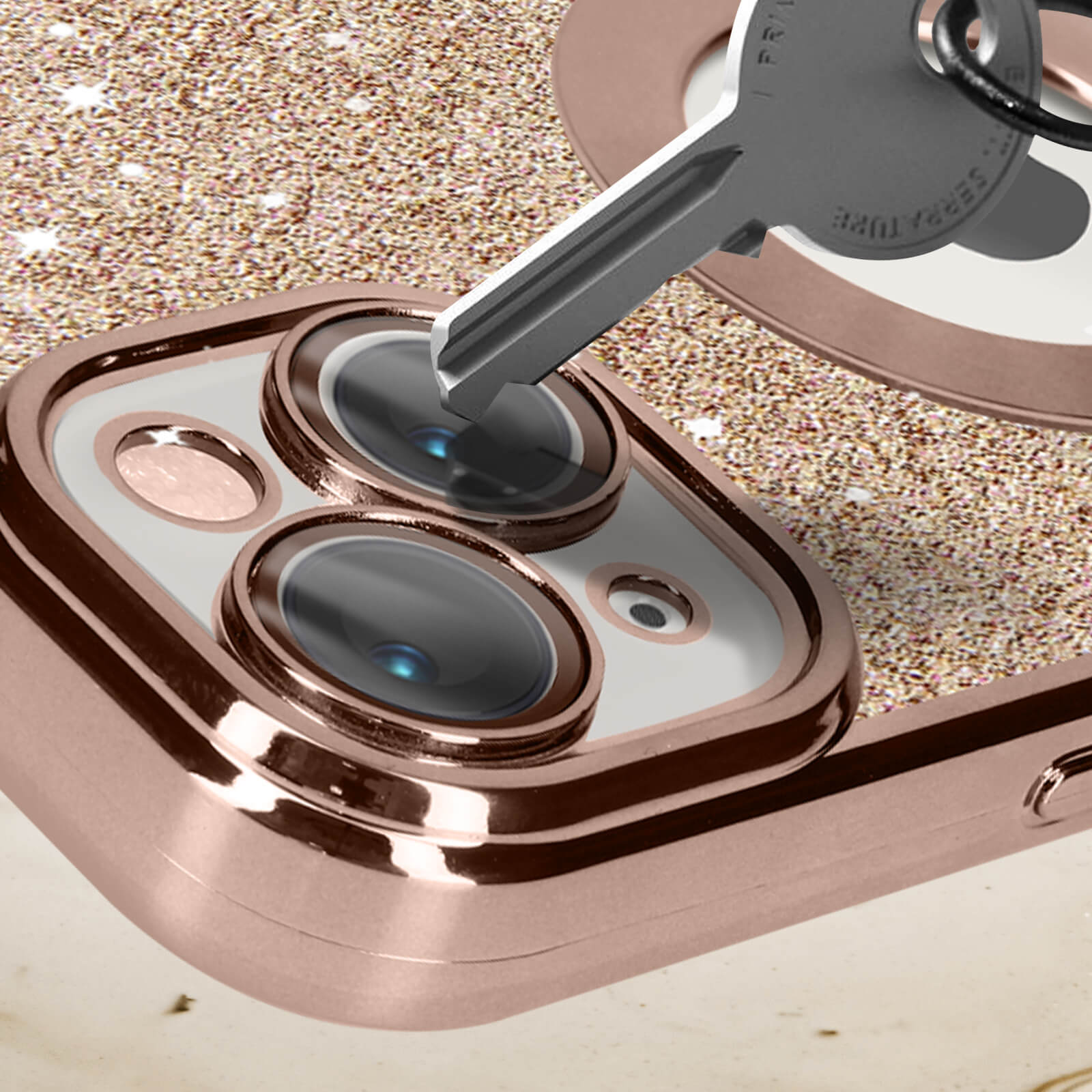 Una chiave viene inserita in una custodia per telefono con un anello per fotocamera in oro rosa e sfondo glitterato.
