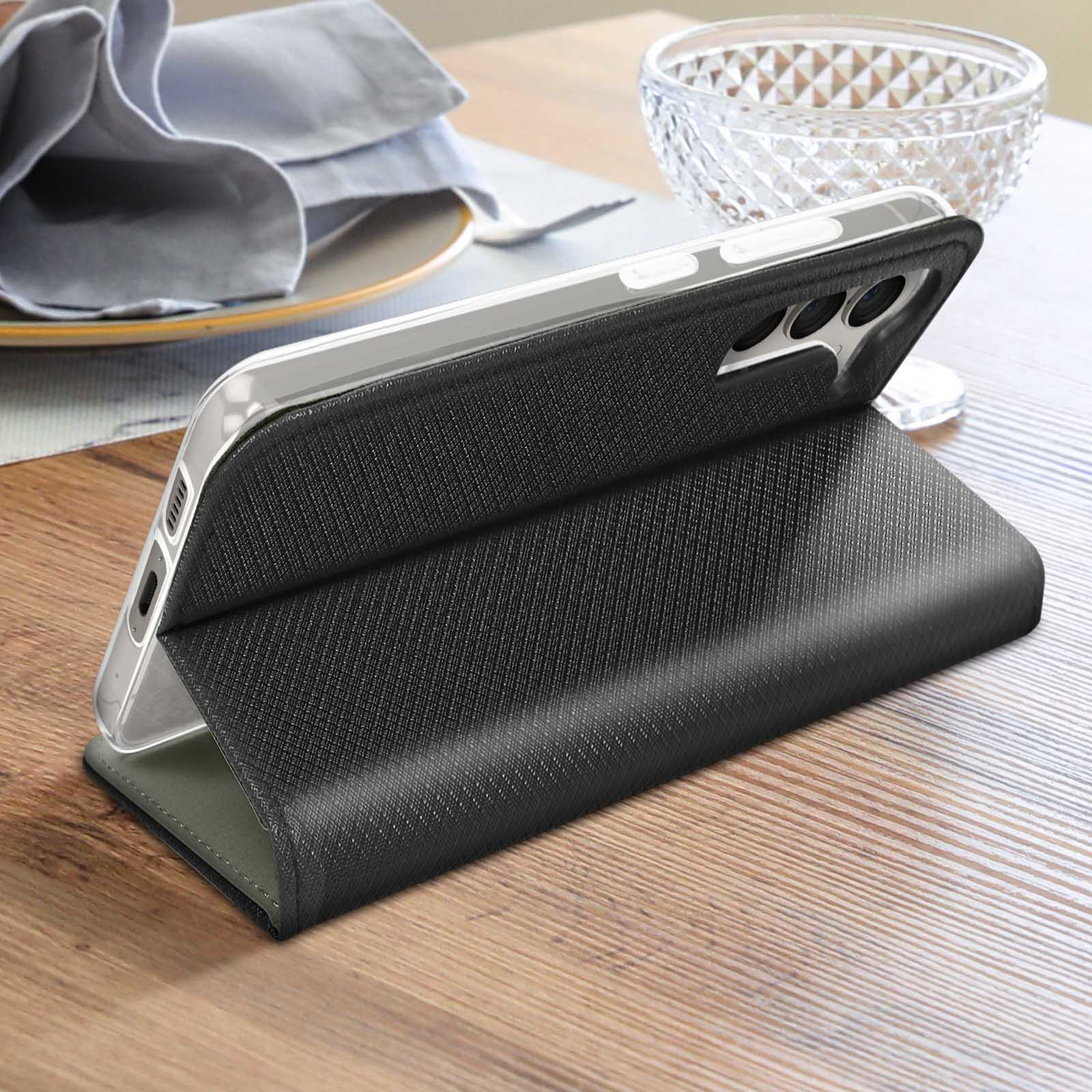 Ein schwarzes Telefon in einer Klapphülle, das auf einem Holztisch liegt, mit einer transparenten Schüssel im Hintergrund.