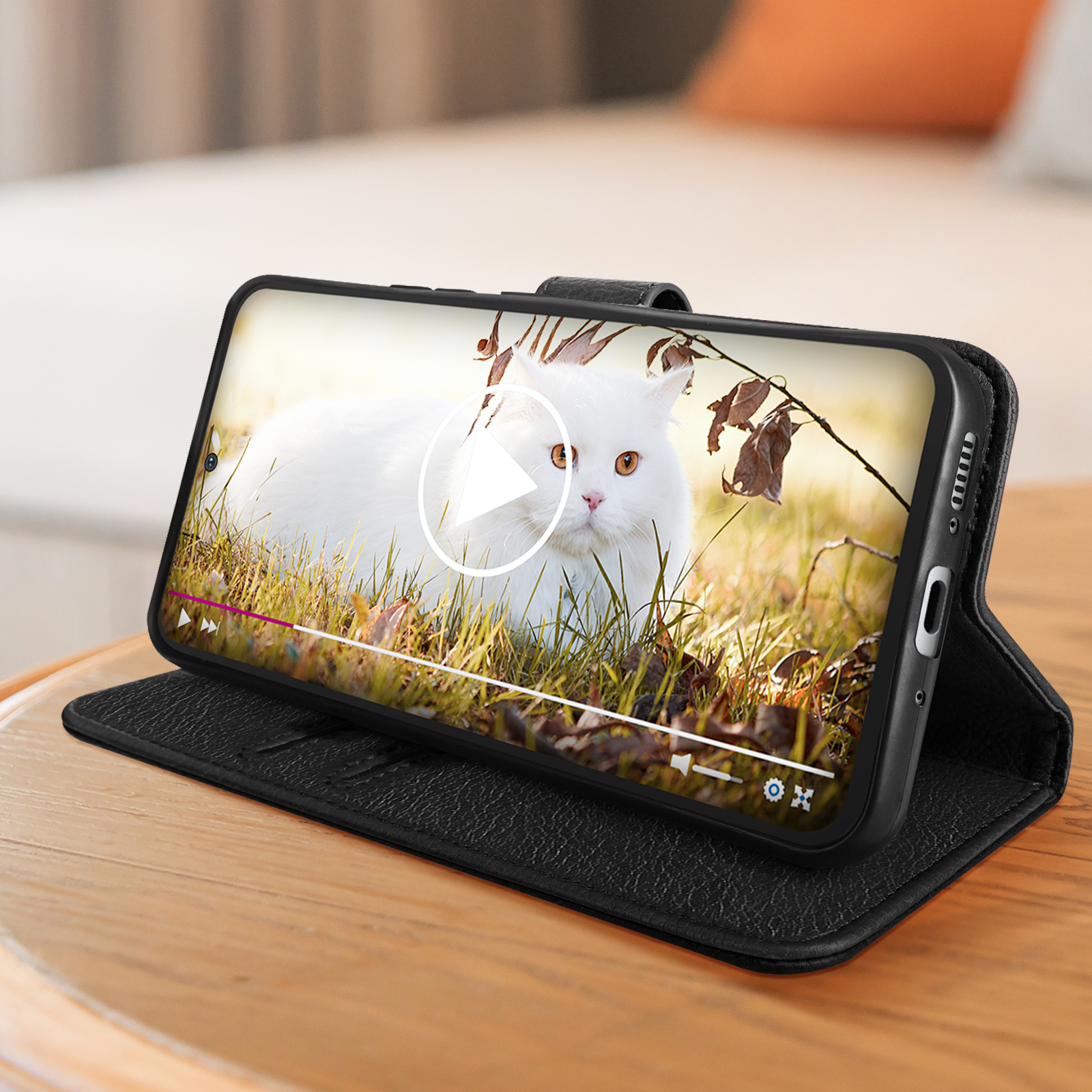 Telefono nero in una custodia di pelle nera, che riproduce un video di un gatto bianco in un campo.