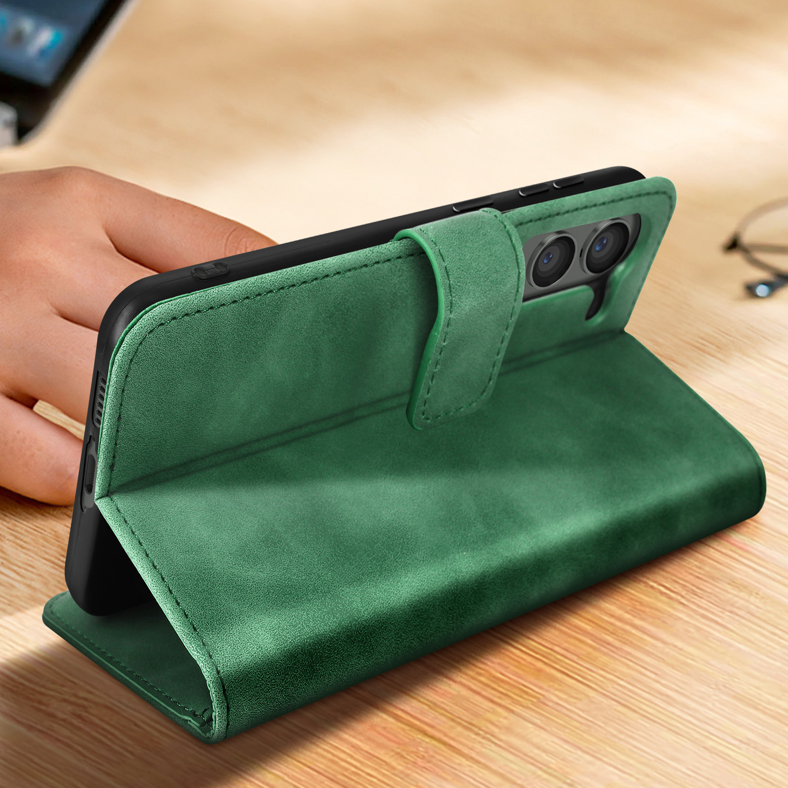 Eine grüne Leder-Handyhülle in der Hand. Das Telefon ist drin, die Hülle offen. Holzoberfläche.