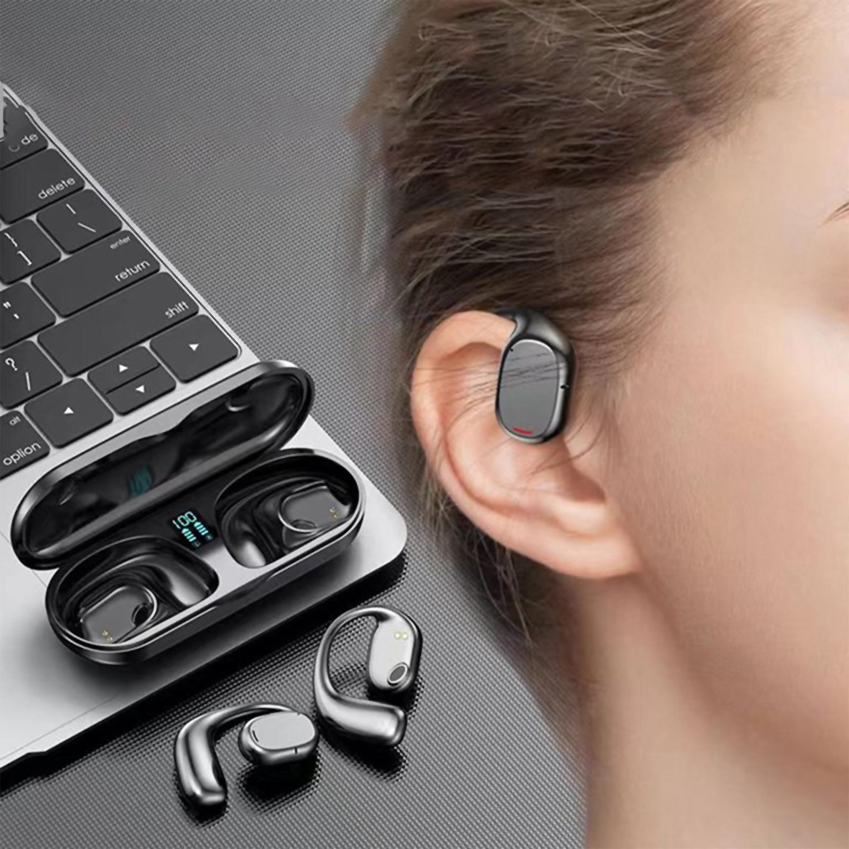 Auriculares en un portátil, uno en la oreja de una persona. Diseño plateado y negro, sobre fondo gris.
