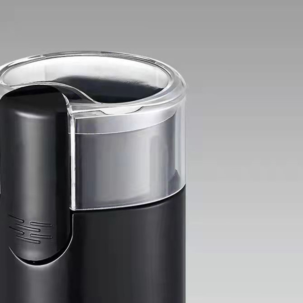 Molinillo de café negro con tapa plateada. El molinillo tiene una tapa transparente y está sobre una superficie gris.