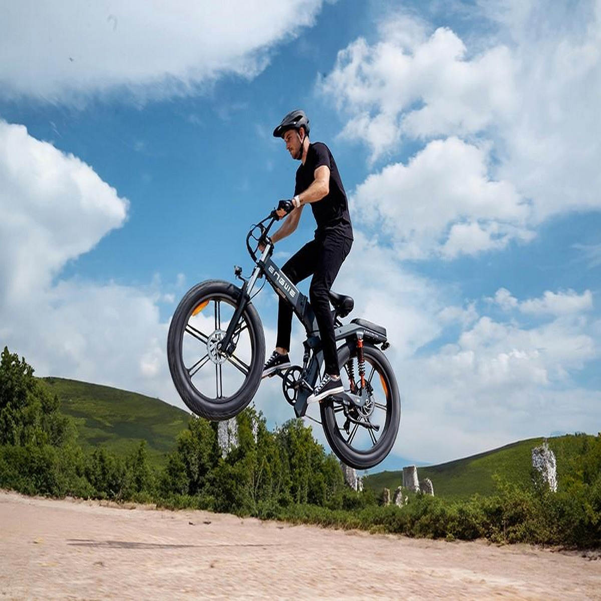 Un uomo in sella a una e-bike che salta in aria. Colline verdi e cielo blu sullo sfondo.