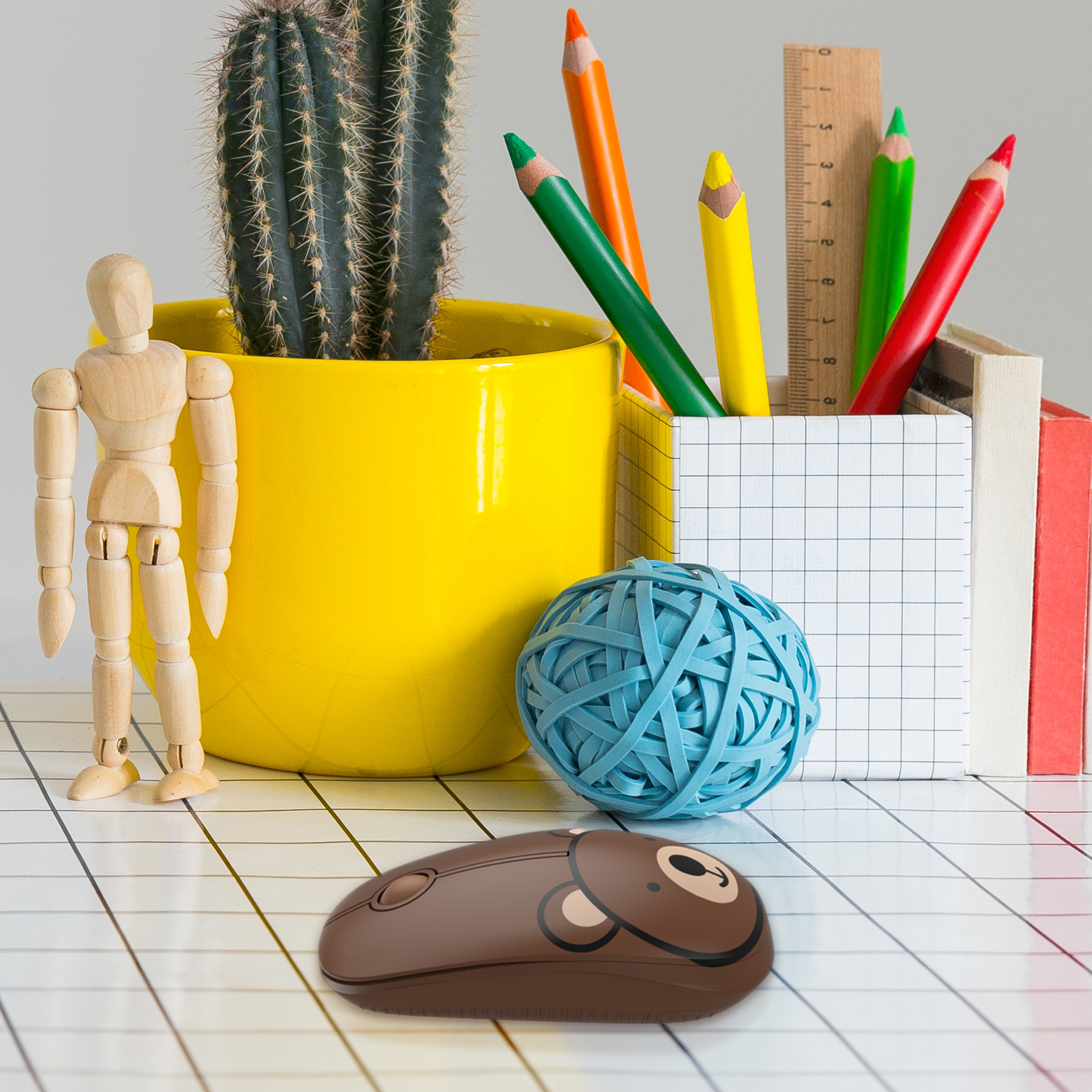 Artystyczna ekspozycja materiałów biurowych. Zawiera ołówki, kaktus, drewnianą lalkę i niebieską kulę z gumek.