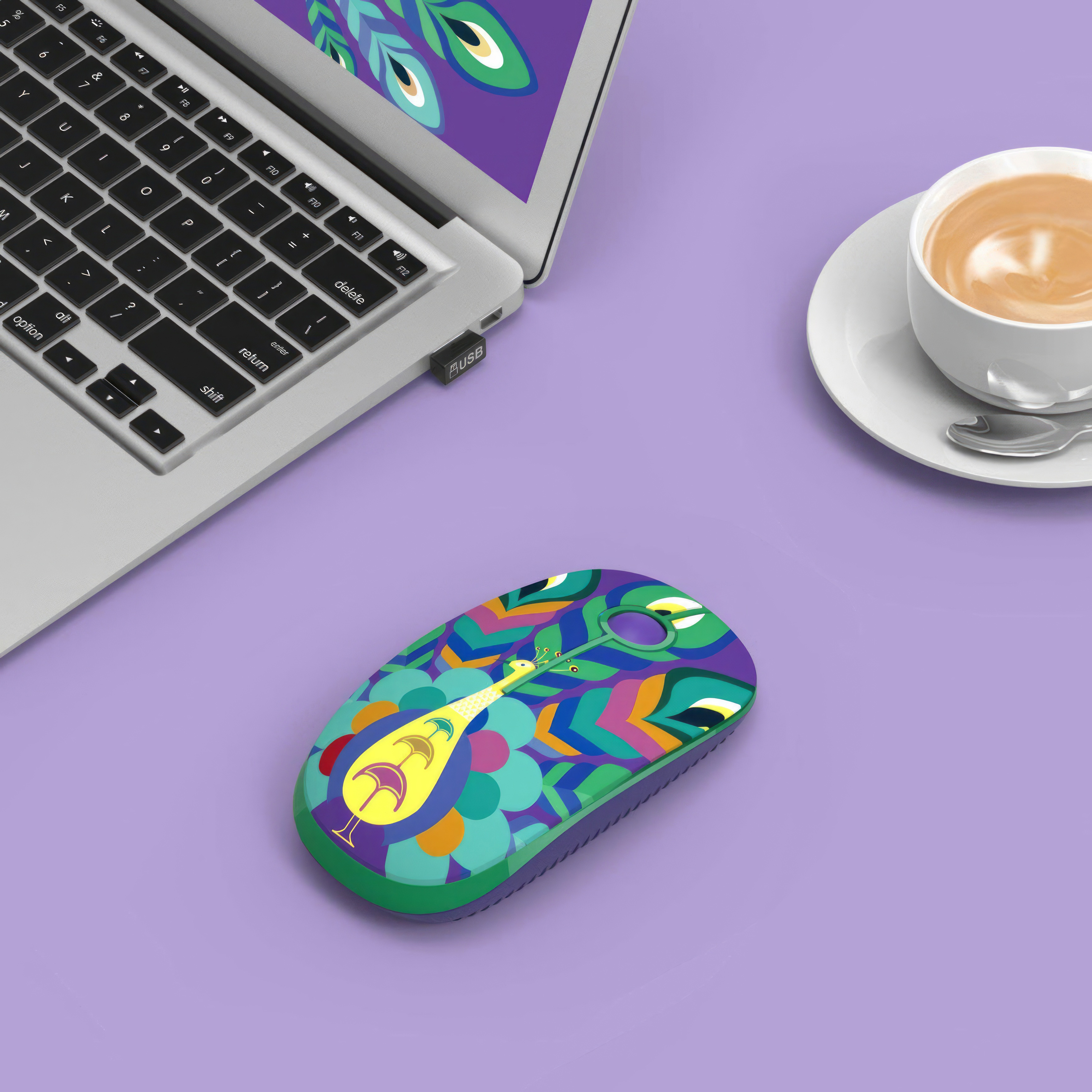 Kolorowa mysz na fioletowej powierzchni obok laptopa i filiżanki kawy.