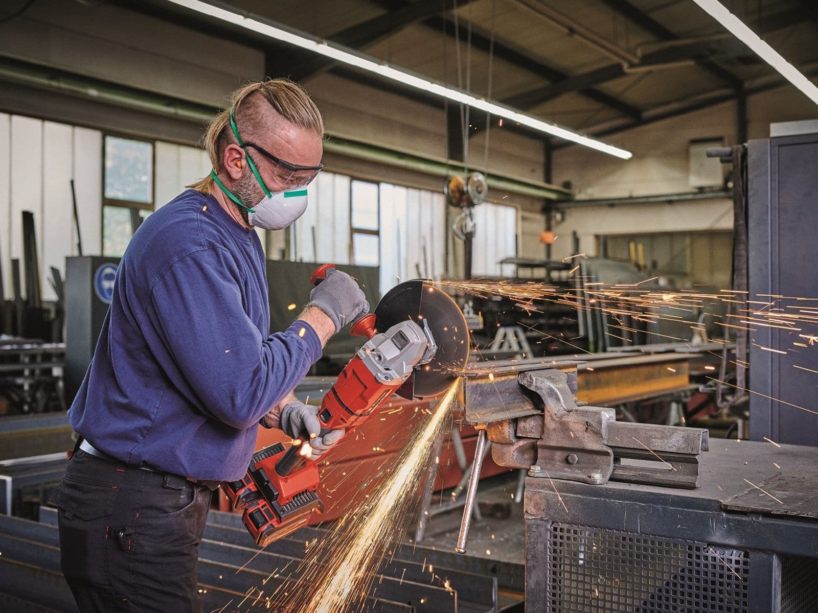 Mężczyzna używa szlifierki kątowej, iskry, odzież ochronna, w warsztacie.