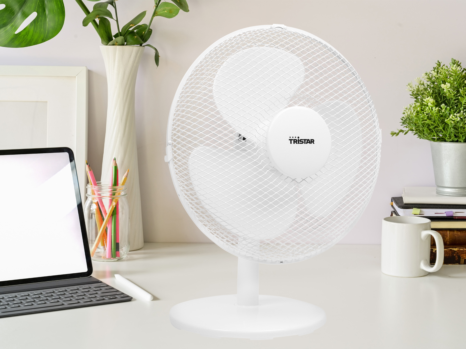 Weißer Tischventilator mit weißem Sockel und Schutzgitter, auf einem Schreibtisch.