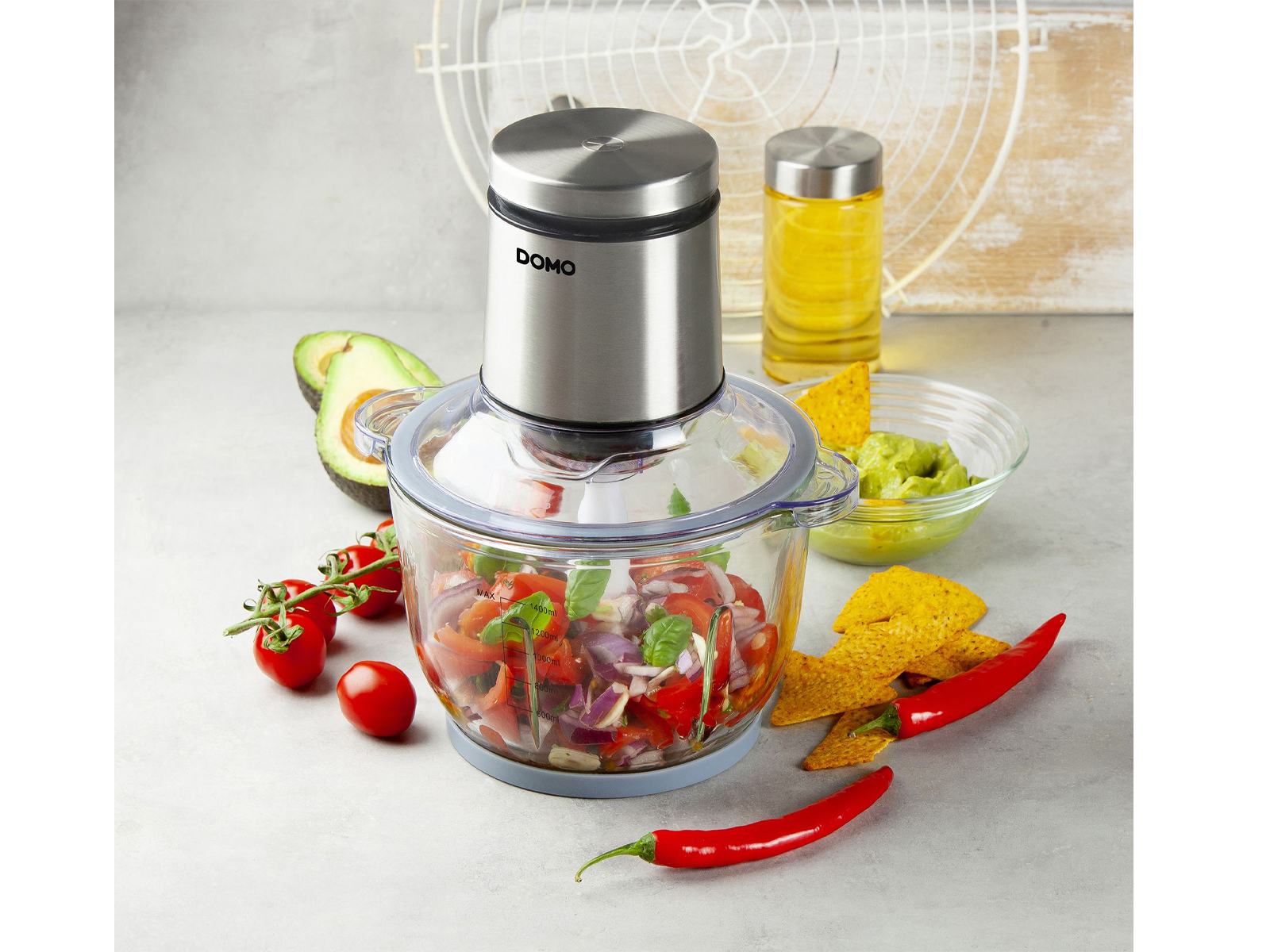 Un robot da cucina con ingredienti. Pomodori, cipolla rossa, avocado, patatine e un bicchiere d'olio.