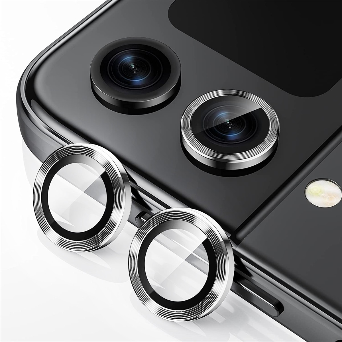 Tre protezioni per lenti della fotocamera argentate, posizionate su un telefono nero, con vetro lucido.
