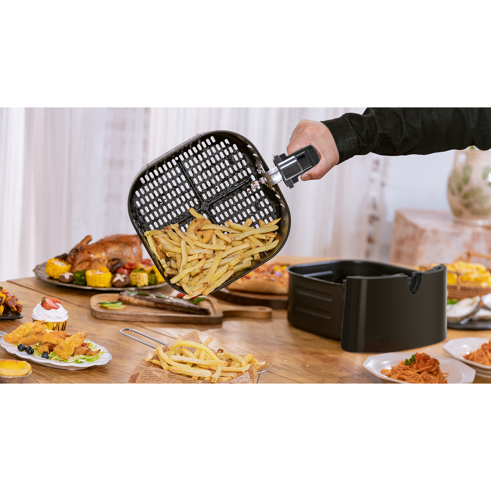Una cesta de freidora llena de papas fritas se sostiene sobre una freidora negra, con varios alimentos en una mesa de madera.