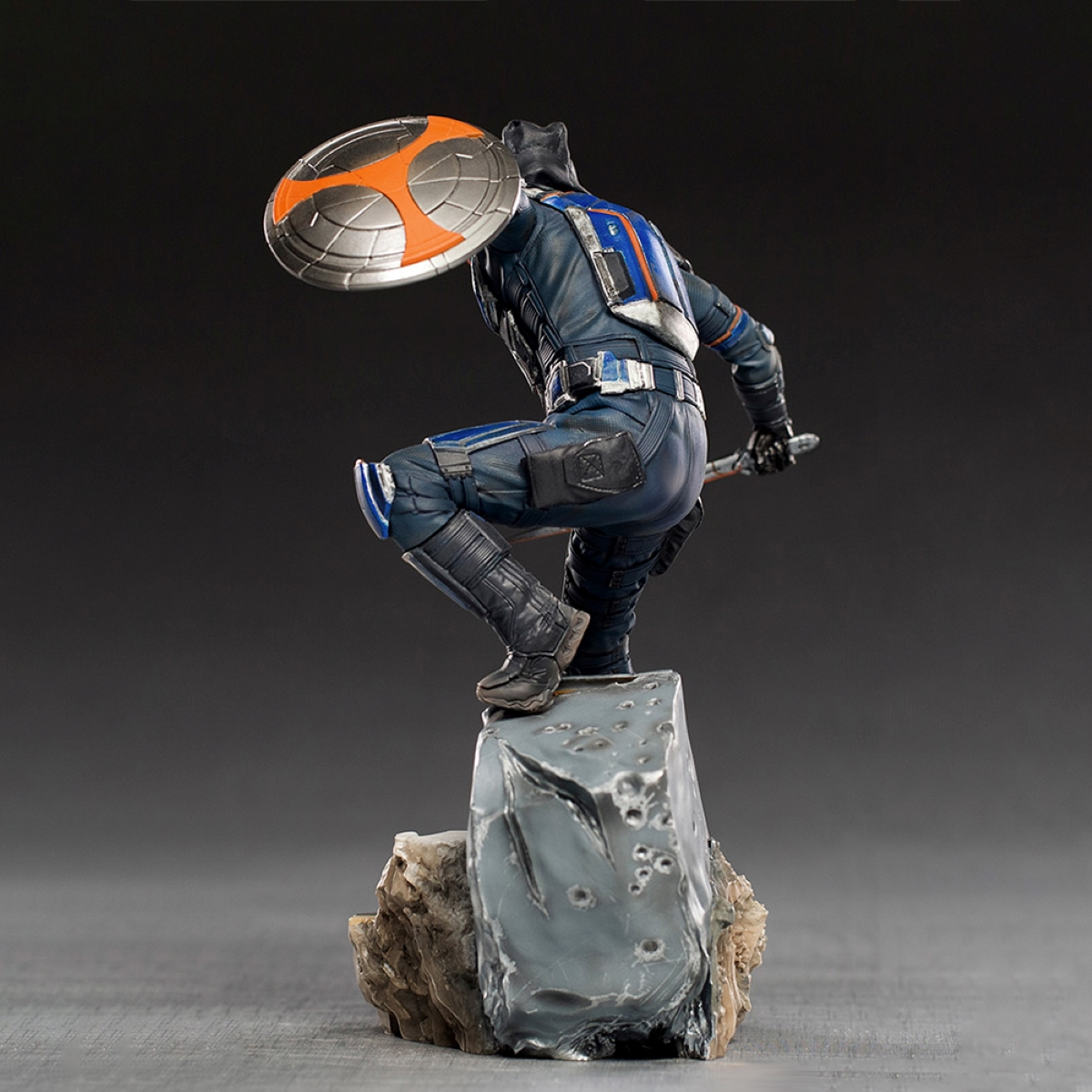 Eine Figur eines Superhelden in einem blau-schwarzen Anzug, der auf einem Felsen kniet.