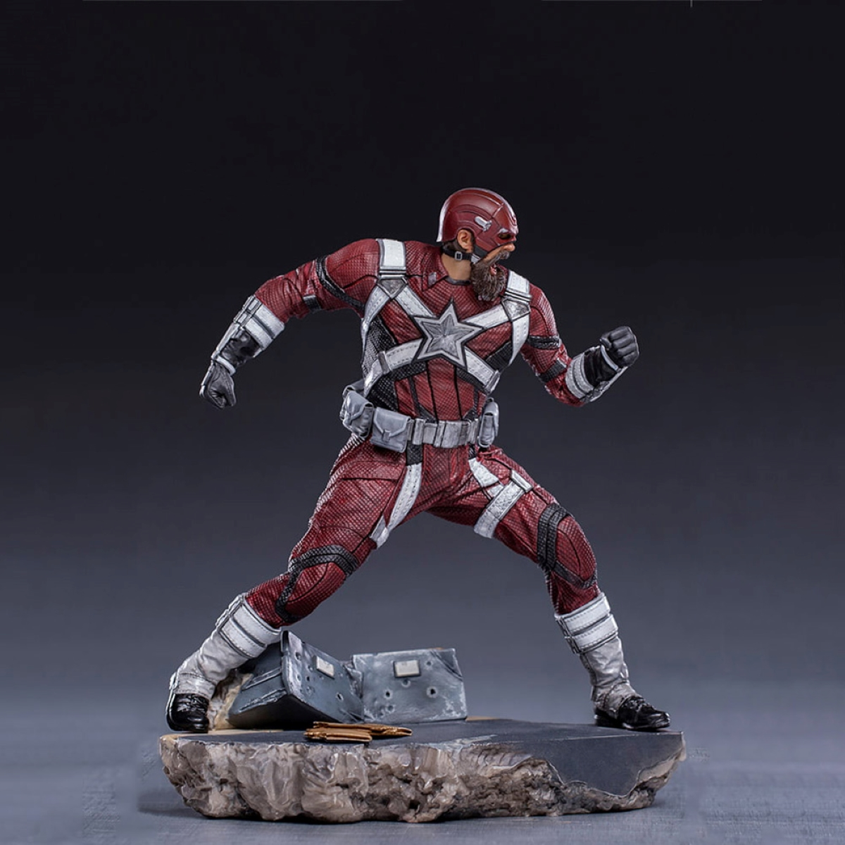 Action figure di un uomo in costume rosso e bianco, posa su una base rocciosa.