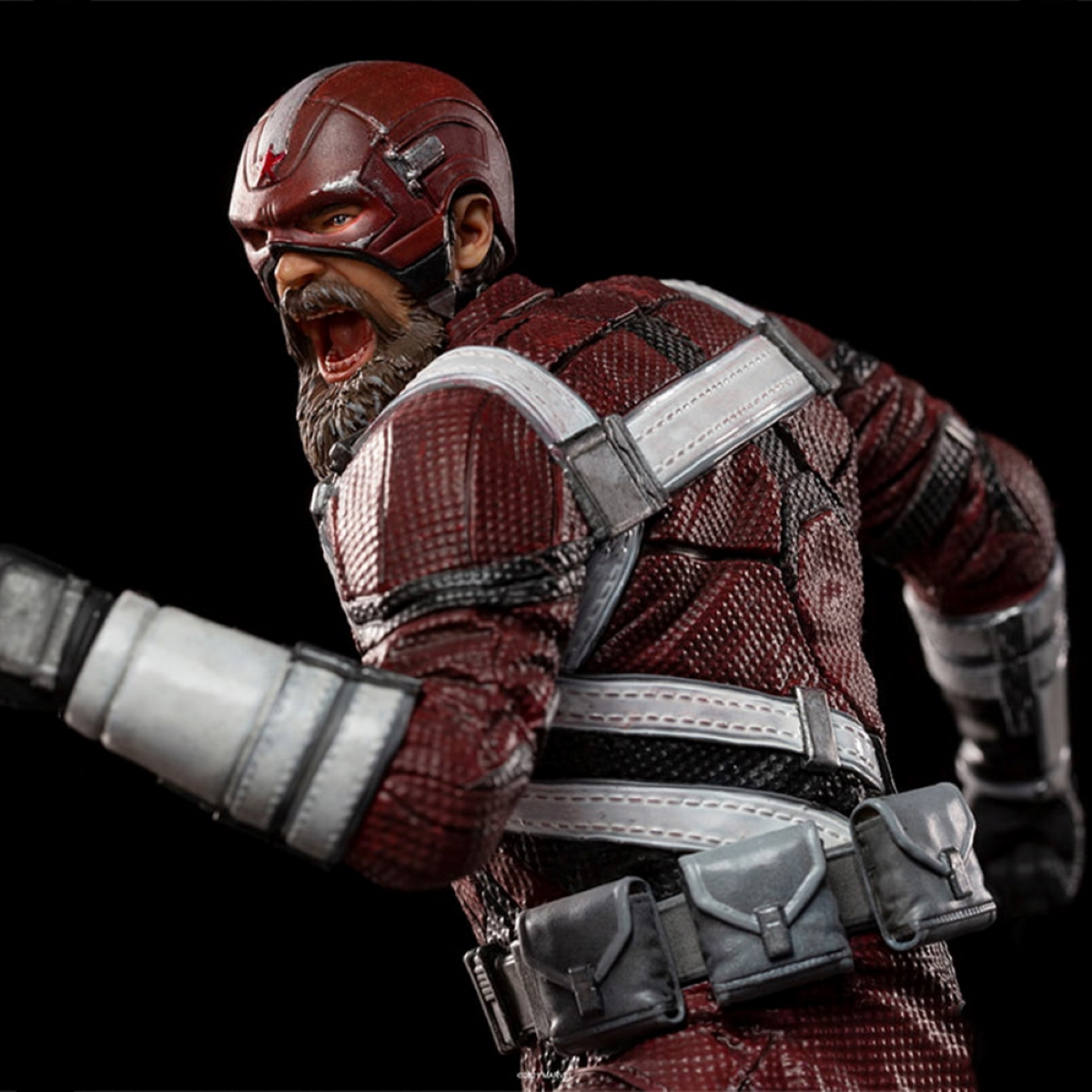Una statua di un uomo con elmetto rosso e barba, che indossa un abito rosso e bianco. Sfondo nero.