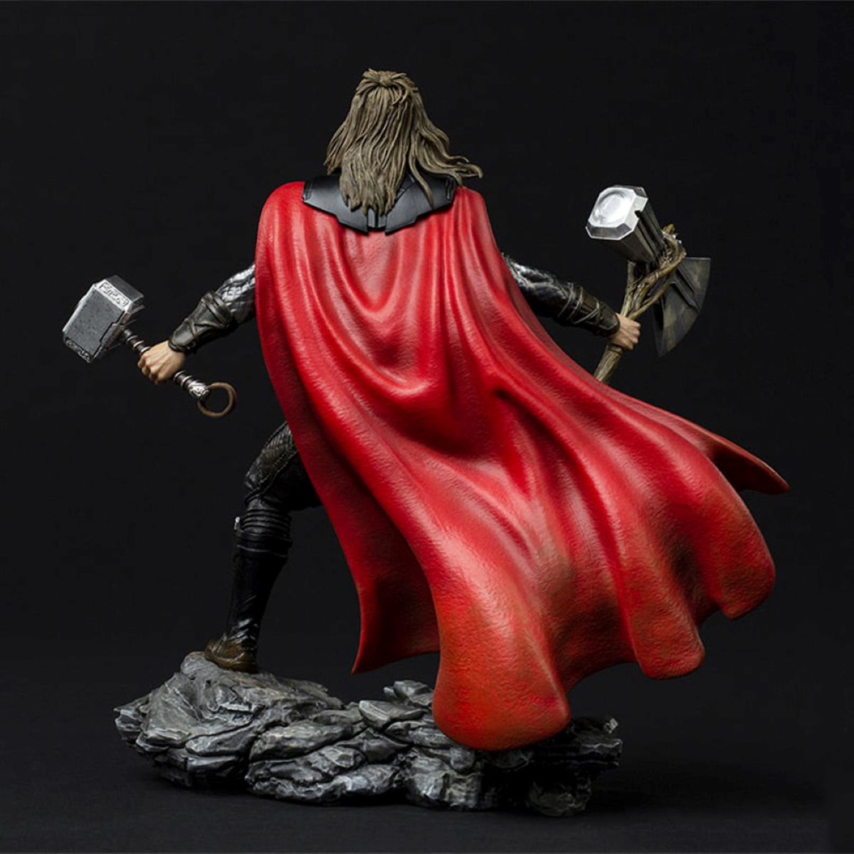 Thor-Statue. Rückansicht. Roter Umhang, hält zwei Waffen, auf Felsbasis.