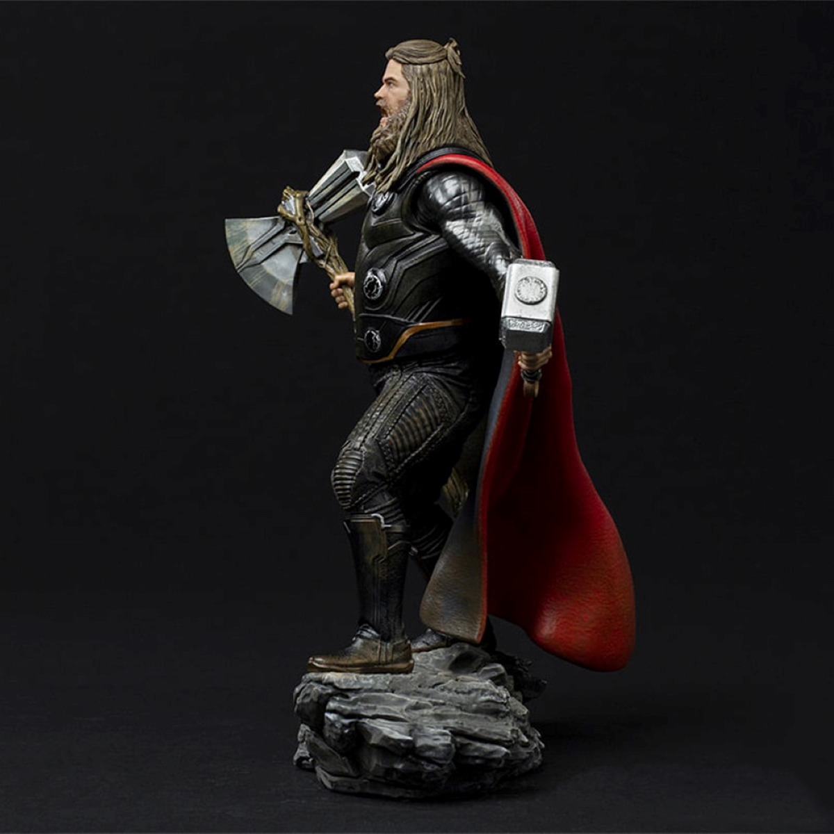Statue von Thor mit Axt und Hammer. Er trägt Rüstung und roten Umhang, auf Felsbasis.