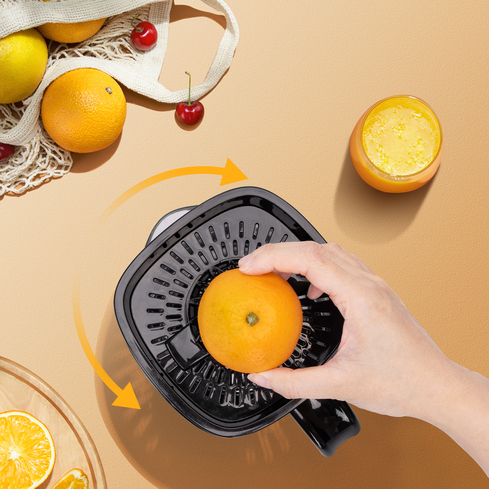 Una mano exprimiendo una naranja en un exprimidor. Zumo de naranja en un vaso. Otras naranjas y cerezas en la mesa.