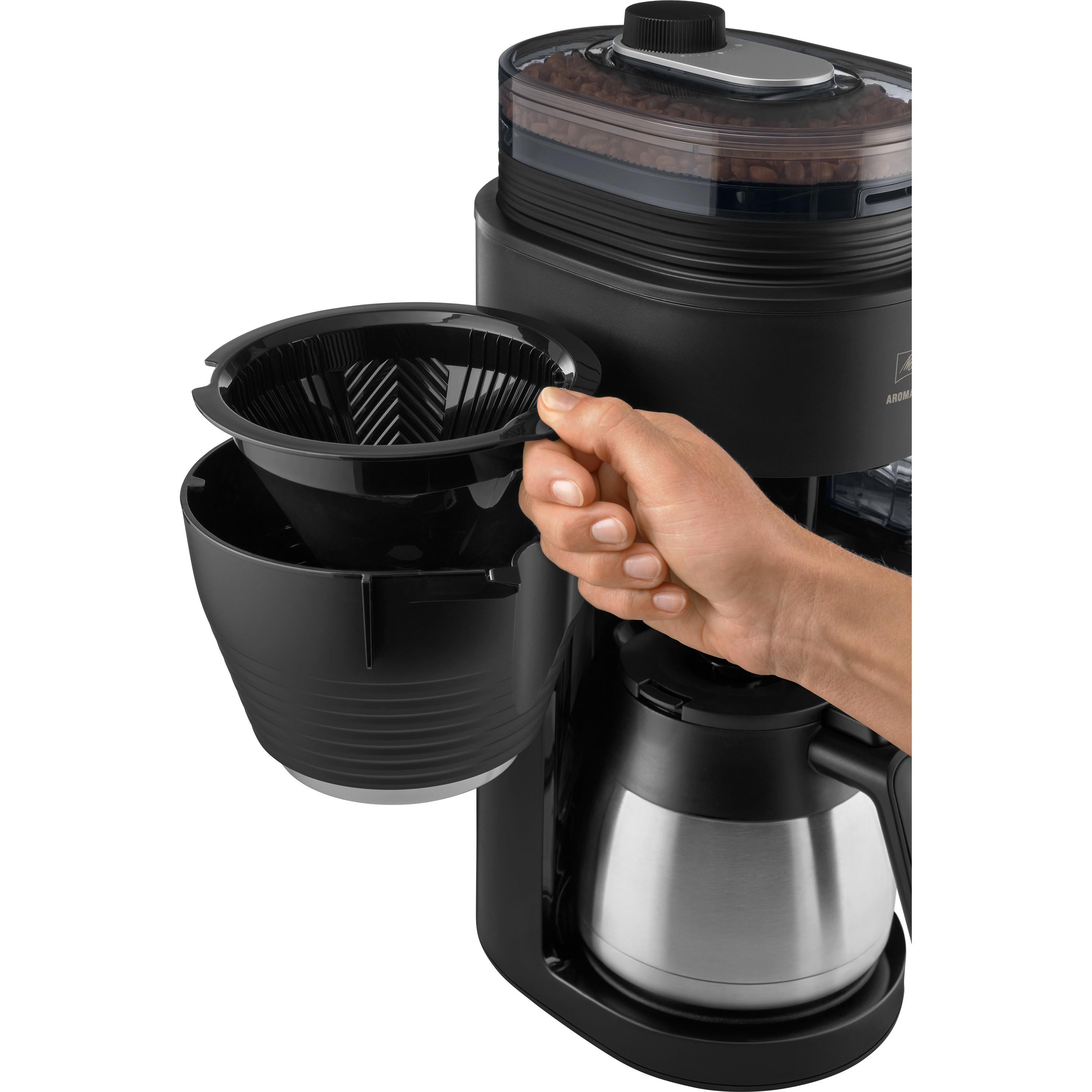 Dłoń osoby trzymająca czarny uchwyt filtra do ekspresu do kawy. Maszyna jest czarna.