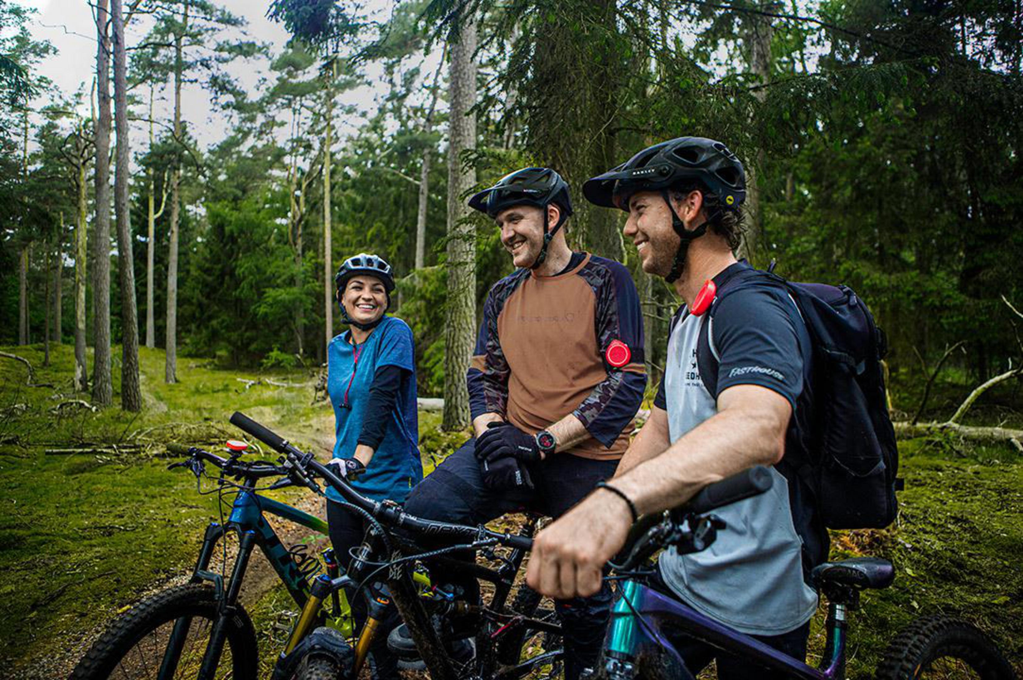 Drei lächelnde Personen mit Fahrrädern in einem Wald. Sie tragen Helme und Freizeitkleidung.