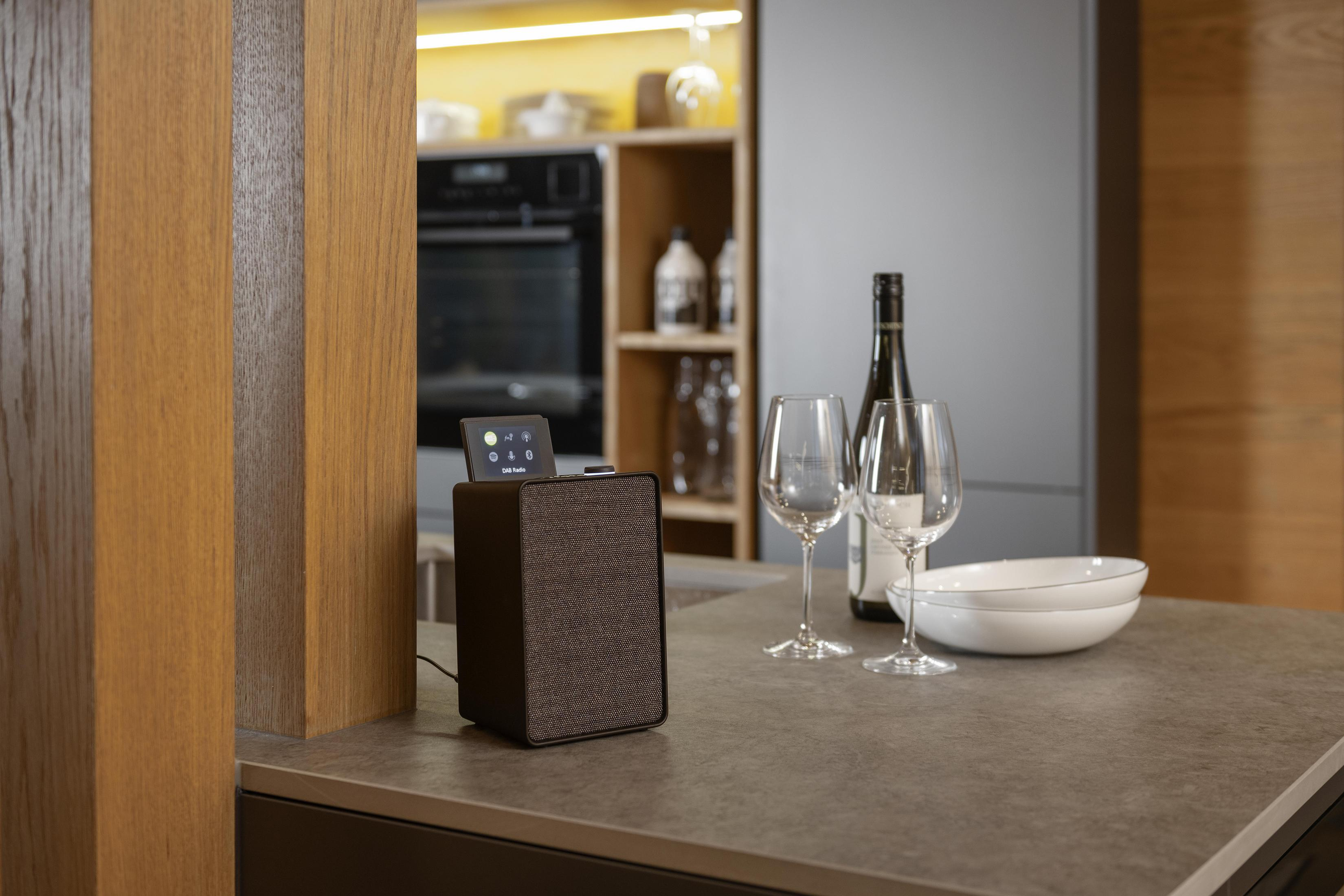 Cucina moderna con altoparlante, bicchieri, vino e ciotola. Lo sfondo mostra mobili e il layout.