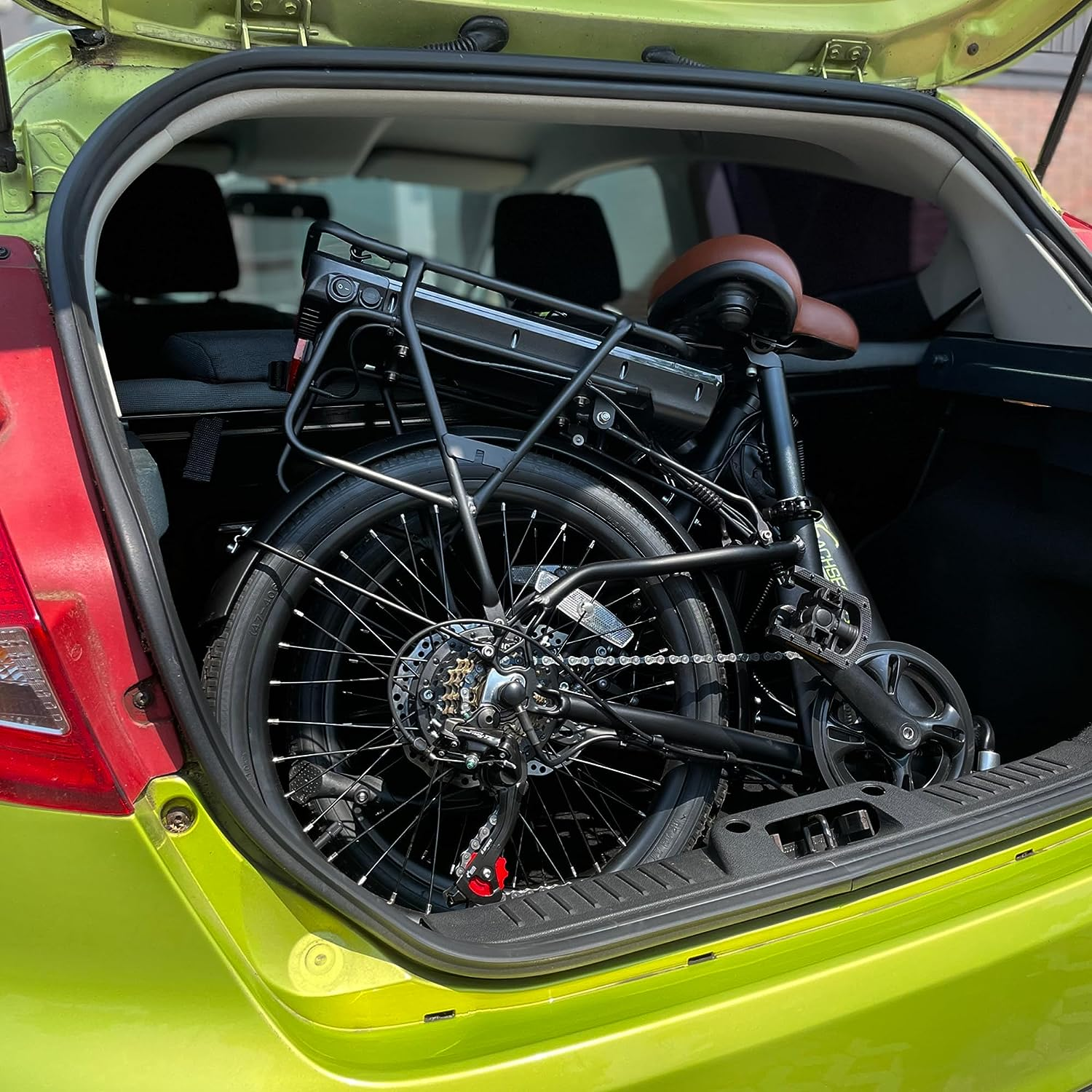 Zusammengeklapptes schwarzes Fahrrad im grünen Kofferraum eines Autos. Brauner Sitz.