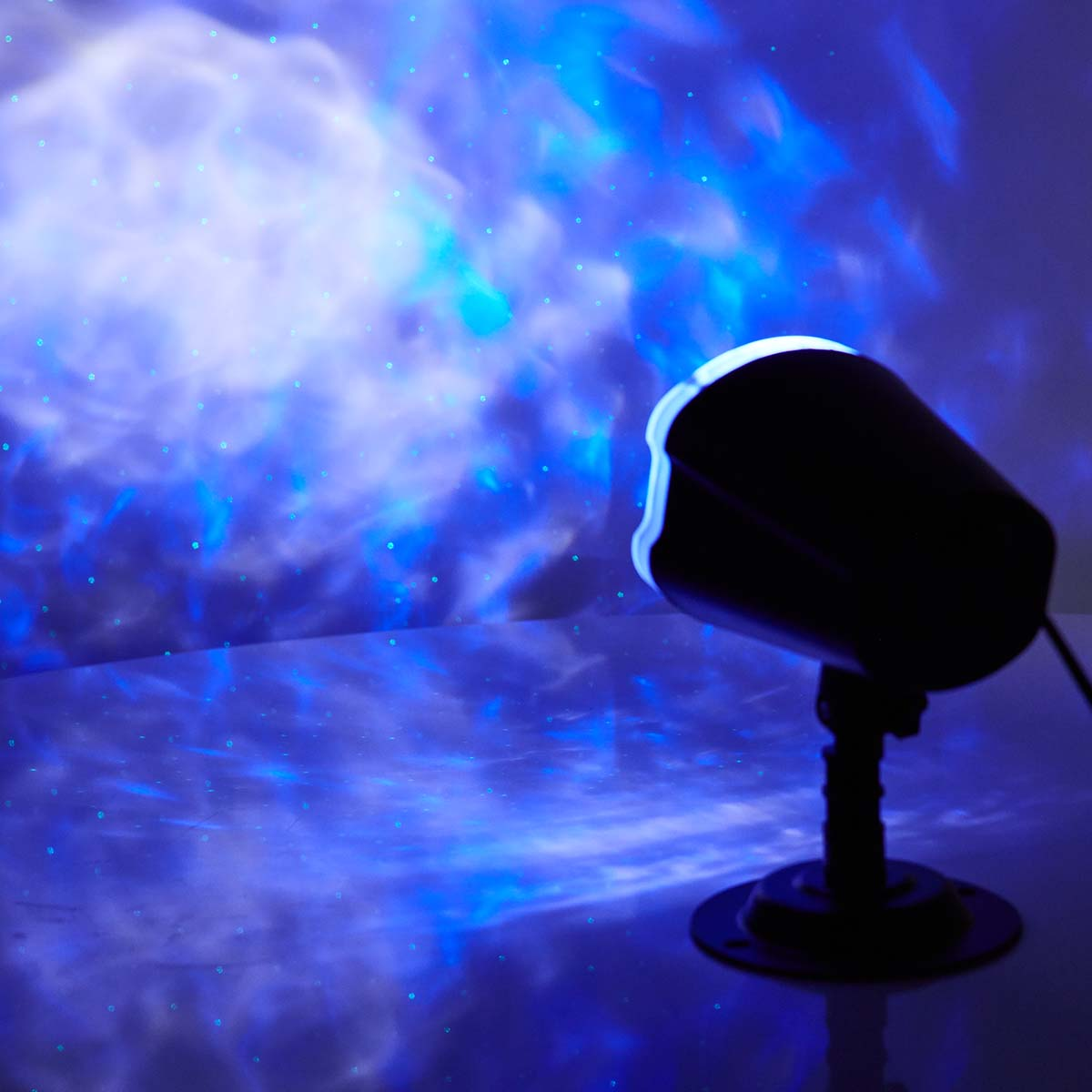 Projektor, der blaues Licht und Punkte auf eine Oberfläche emittiert, wodurch ein Sternenhimmel-Effekt entsteht.