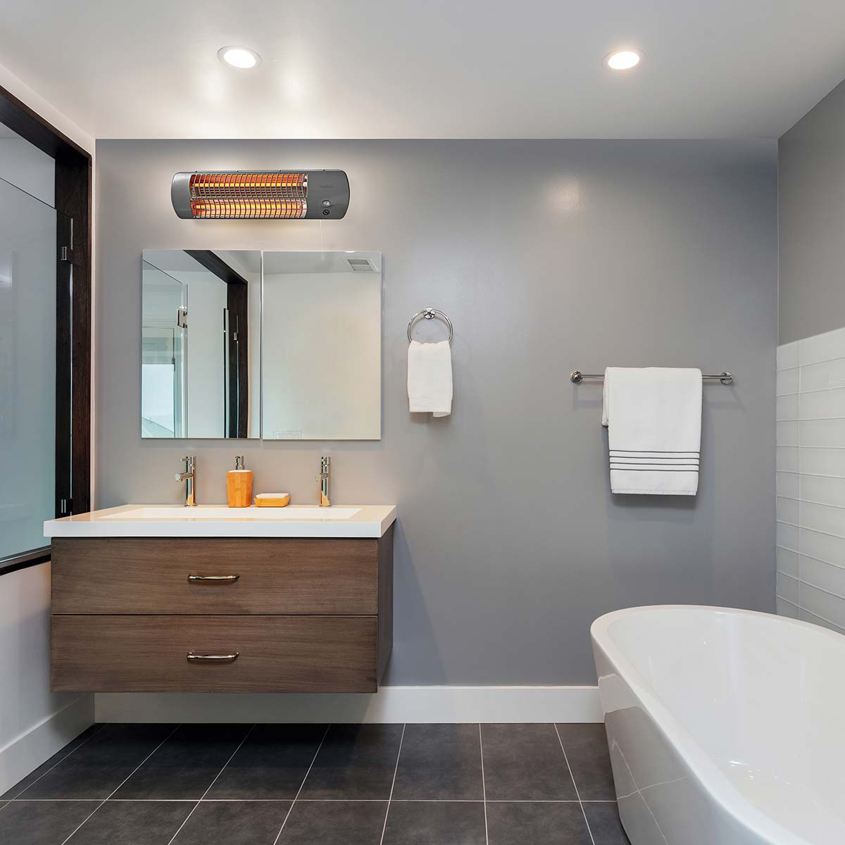 Badezimmer mit beheiztem Handtuchhalter, Spiegel, Waschbecken und Badewanne. Graue Wände und dunkler Fliesenboden.