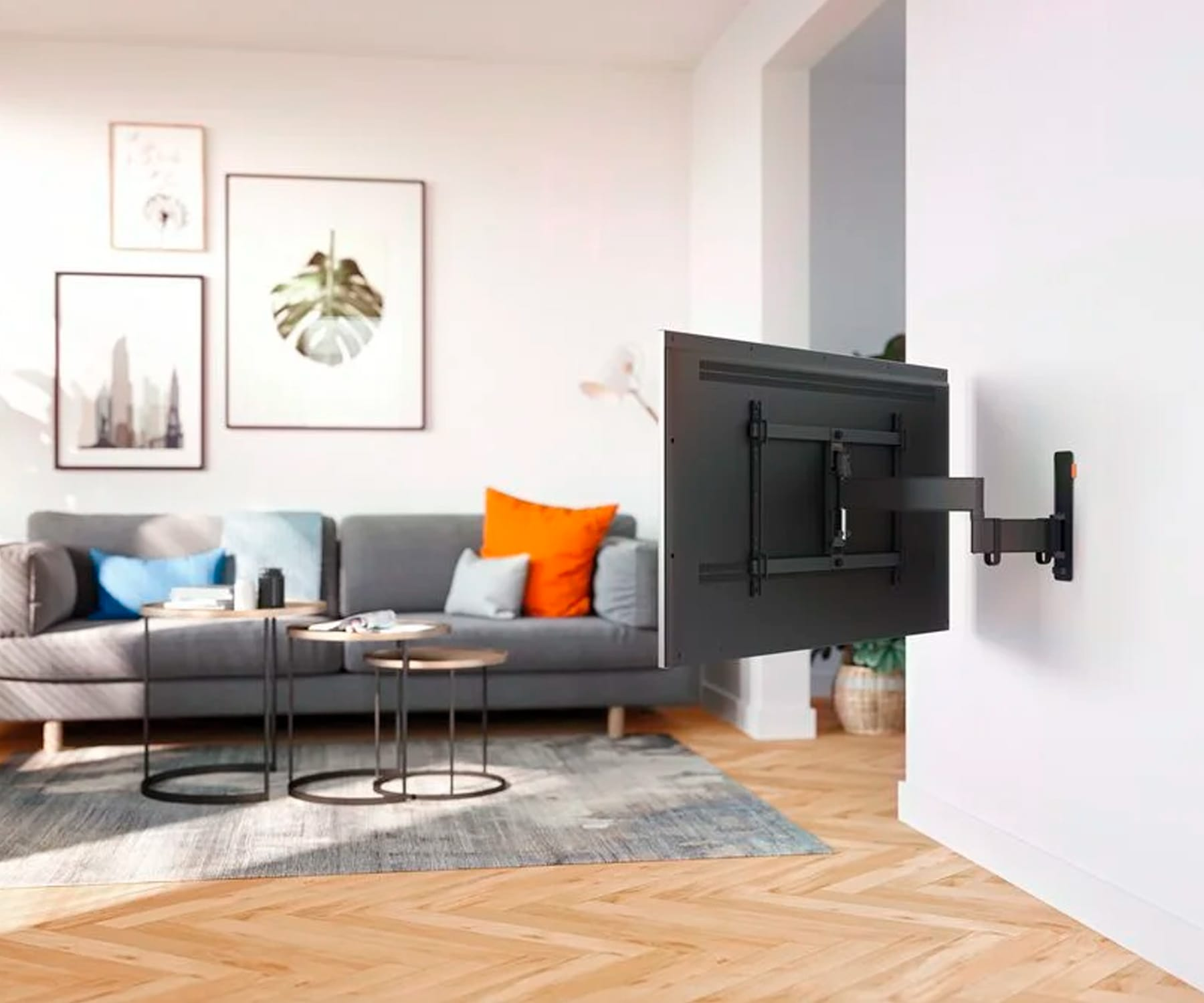 Telewizor jest zamontowany na ścianie. Szara sofa i stoliki kawowe są na pierwszym planie.