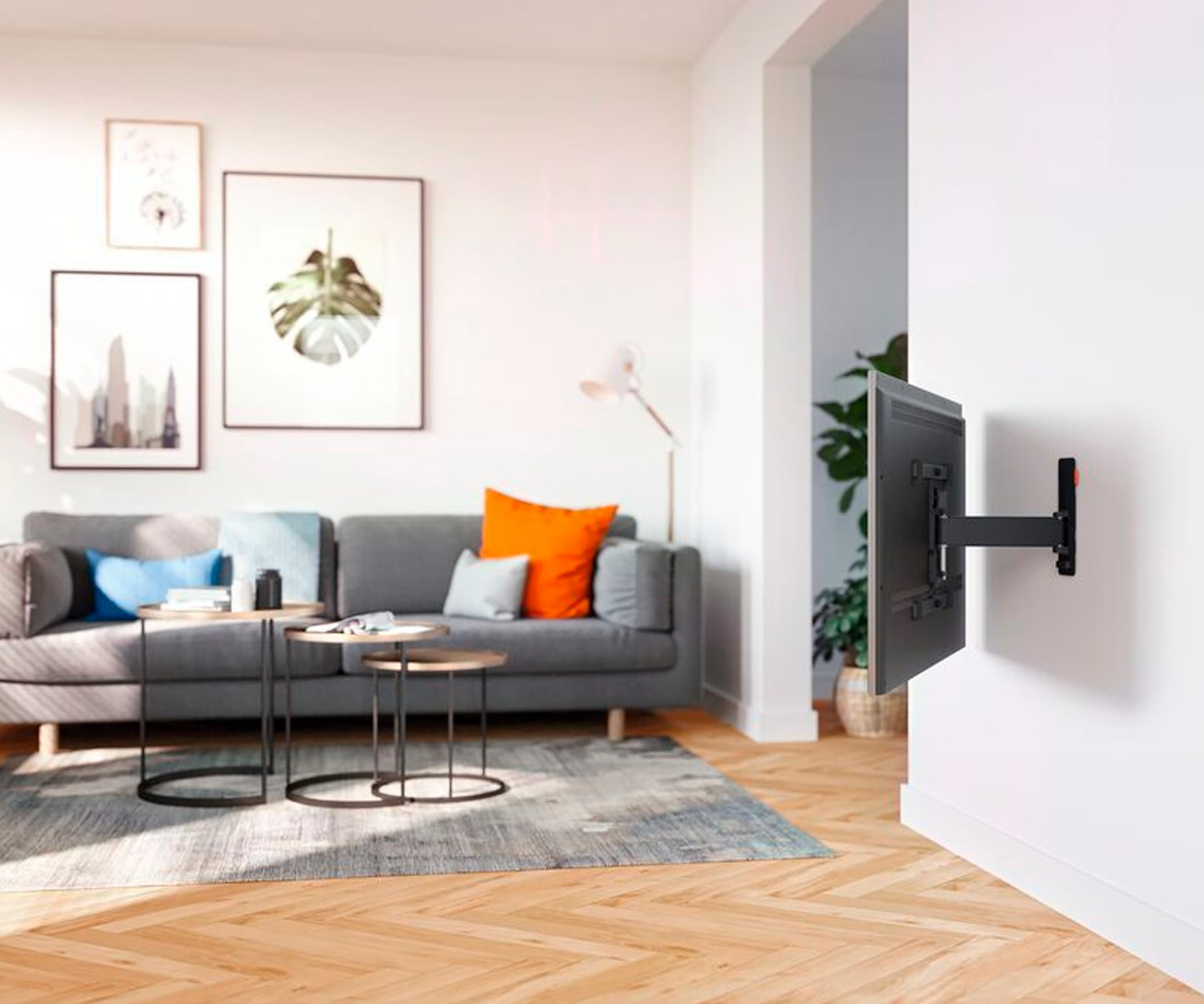 Una sala de estar con un televisor montado. Hay un sofá gris, dos mesas y arte en las paredes.
