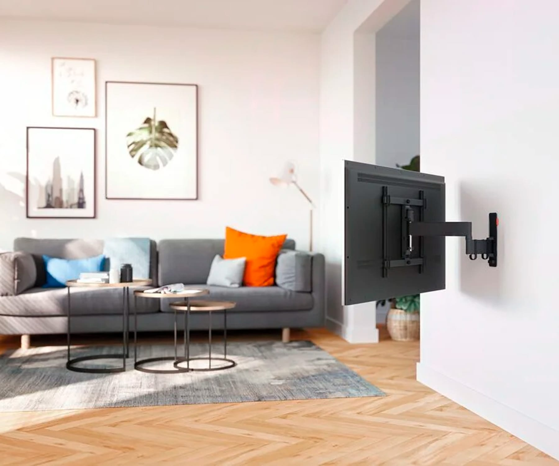 Un televisor montado en una pared, con un sofá, pinturas y una alfombra en una sala de estar.