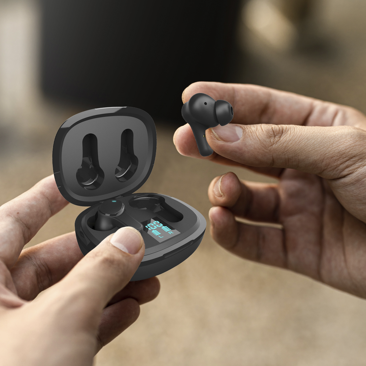 Para czarnych bezprzewodowych słuchawek w etui ładującym. Trzymane w dłoniach, ciemne tło.