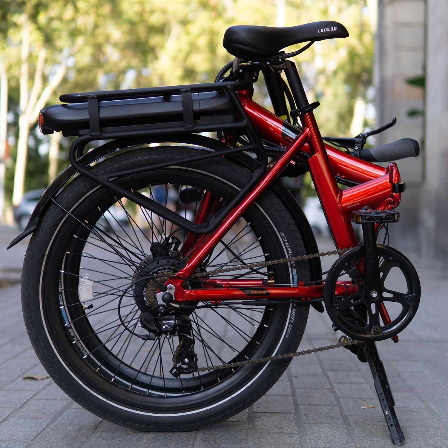 Ein rotes, zusammenklappbares Elektrofahrrad mit schwarzem Sitz und Gepäckträger, geparkt auf einem Bürgersteig.