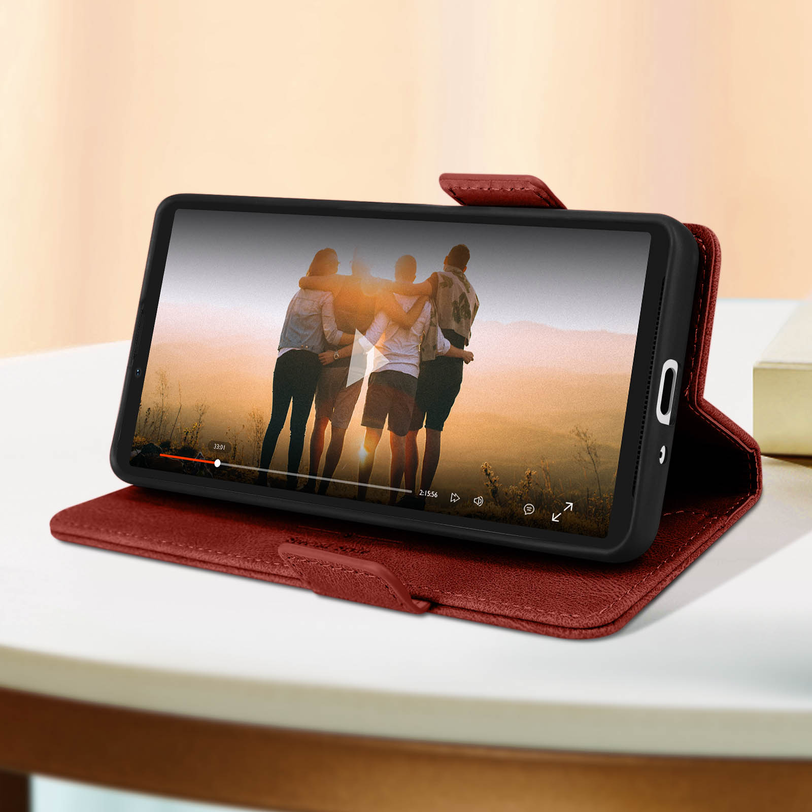 Telefon in roter Hülle zeigt Video von Leuten. Hülle liegt auf weißem Tisch.
