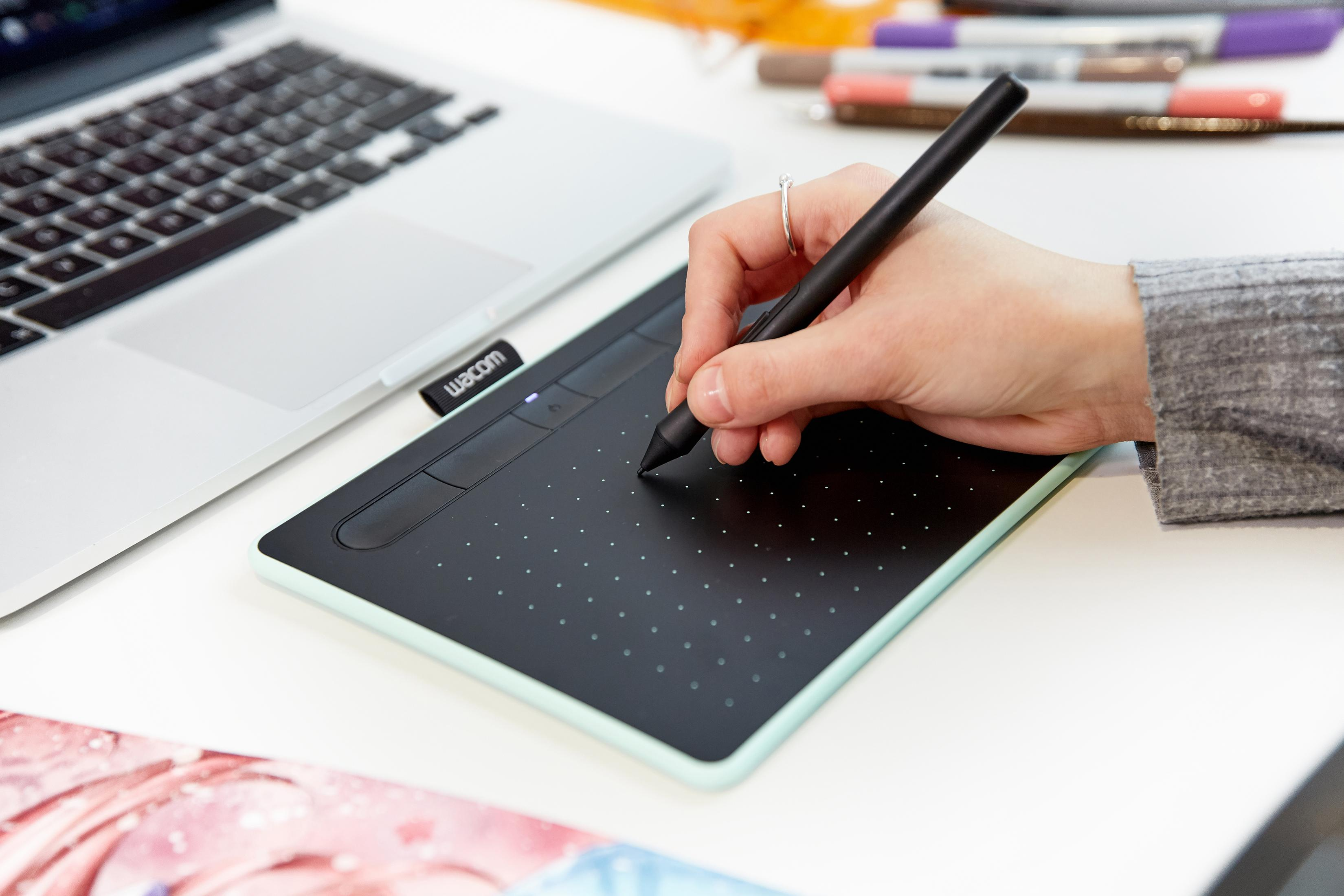 Una persona che disegna su una tavoletta Wacom, con laptop e materiale artistico visibili.