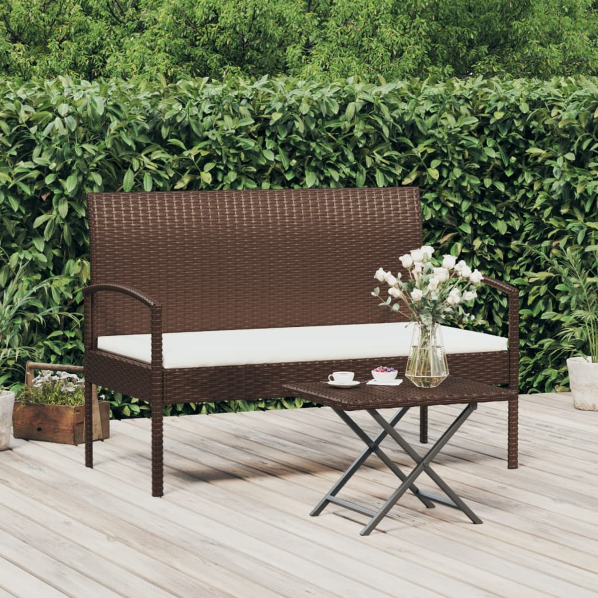 Braune Korbbank mit kleinem Tisch und Blumen. Grüne Hecke im Hintergrund.
