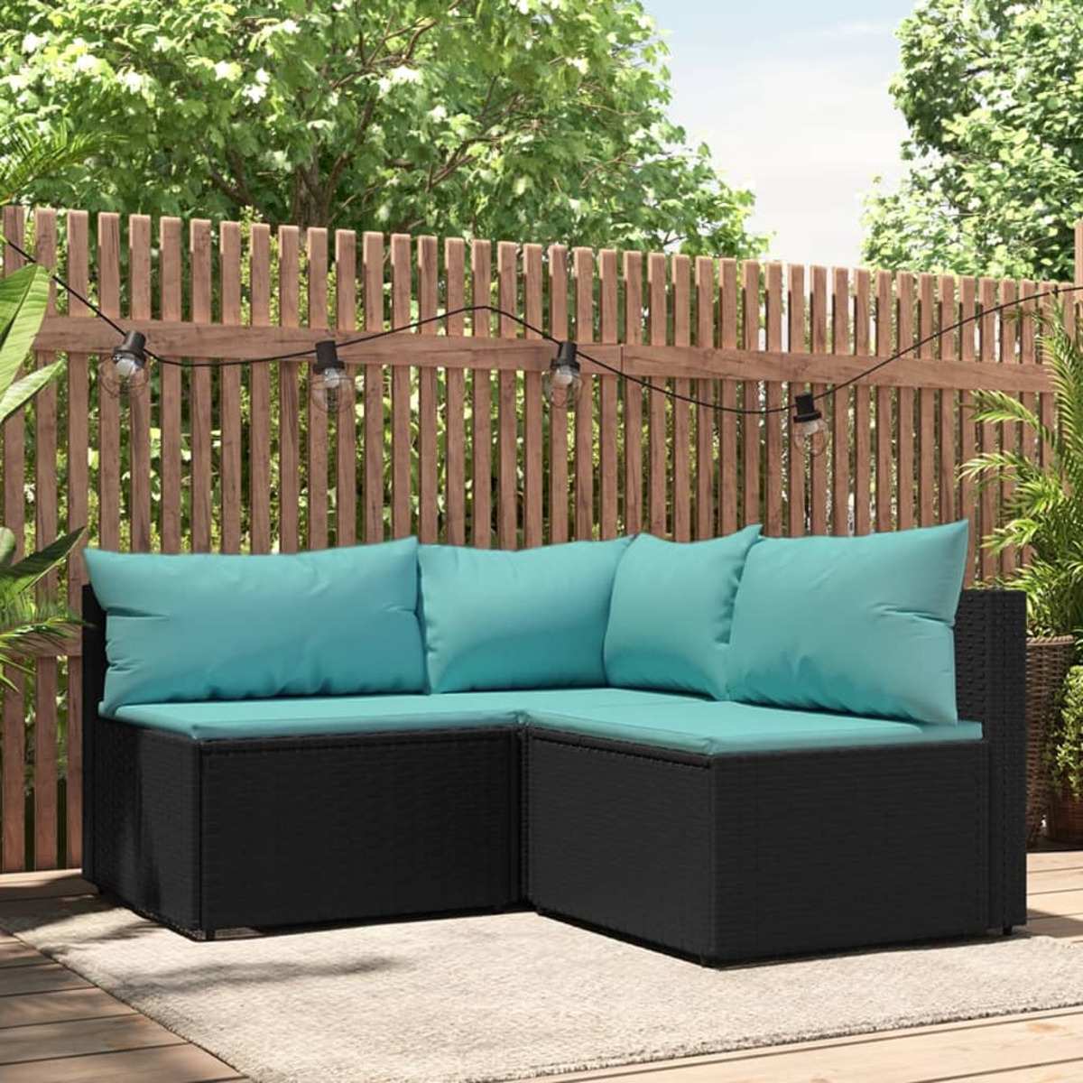 Schwarzes Outdoor-Ecksofa mit türkisfarbenen Kissen. Holzzaun und Lichter im Hintergrund.