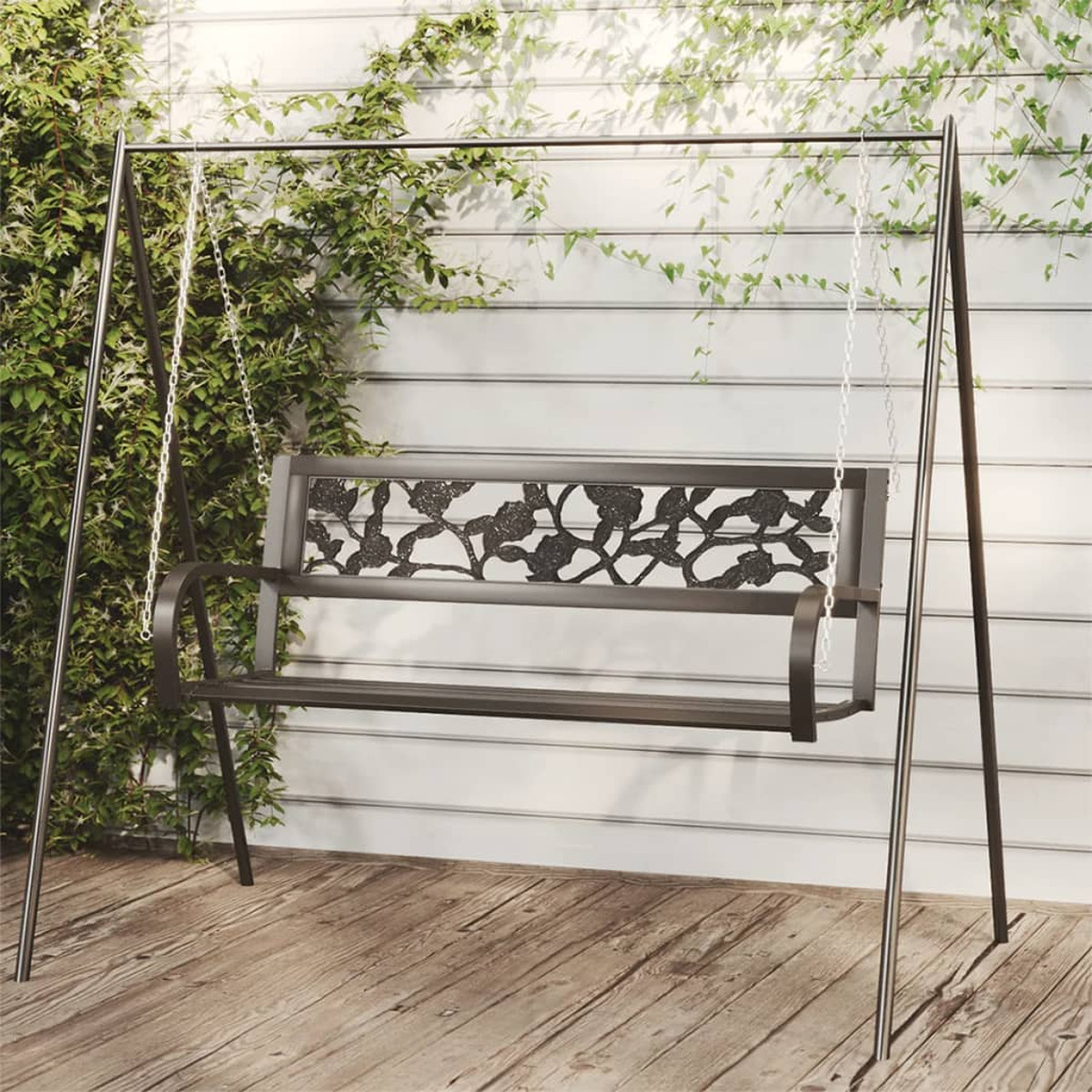 Eine dunkle Metallschaukel mit Blumendesign vor einer weißen Wand mit Ranken.