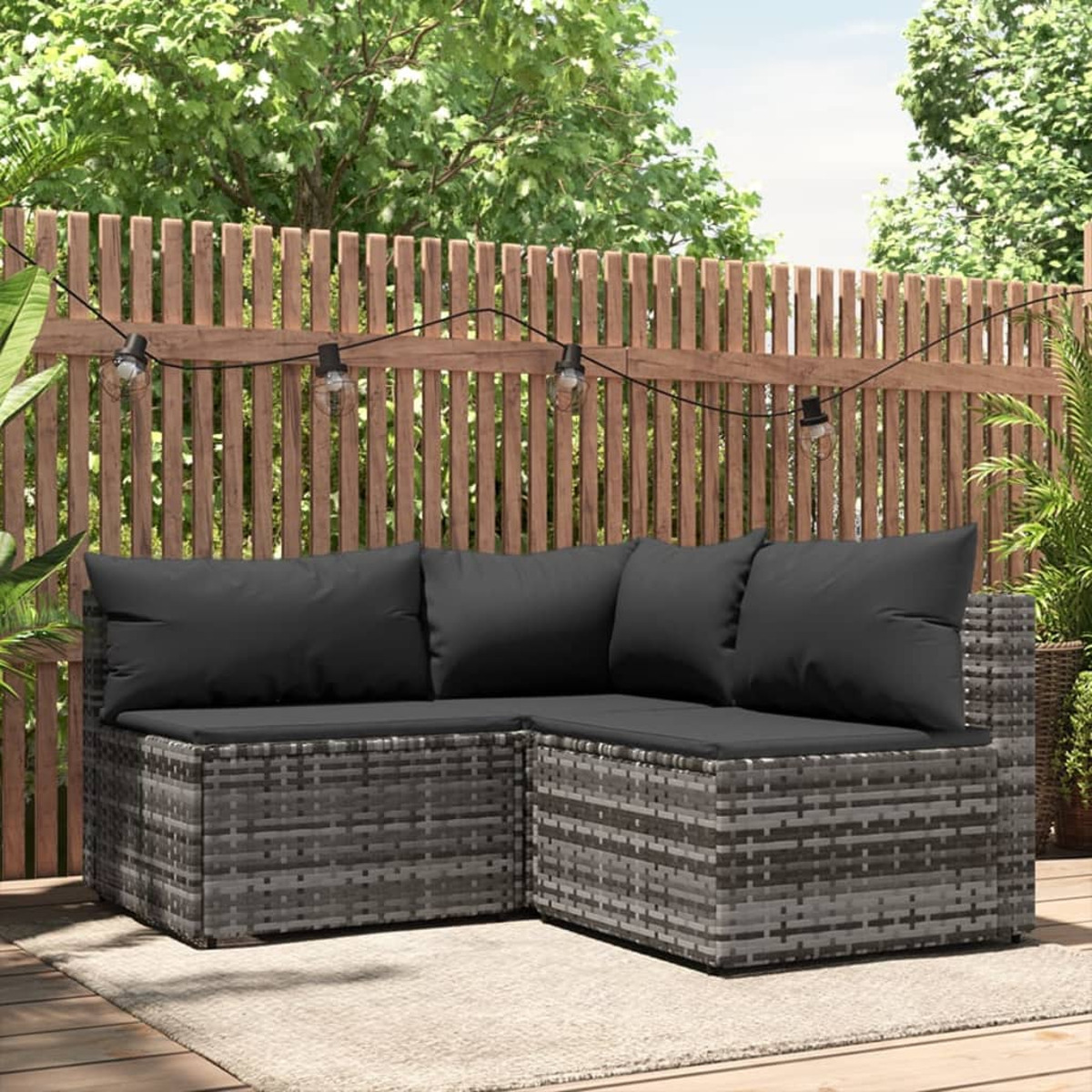 Ein graues Korbsessel-Ecksofa auf einem Holzdeck mit Lichterketten und einem Holzzaun im Hintergrund.