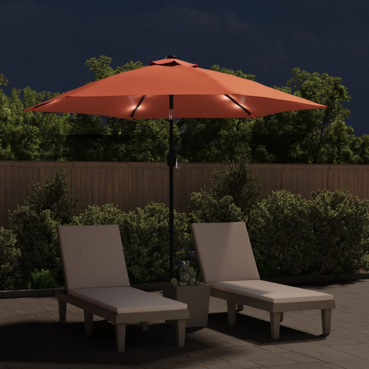 Terrassenszene bei Nacht mit einem orangefarbenen, beleuchteten Sonnenschirm. Zwei Liegestühle darunter.