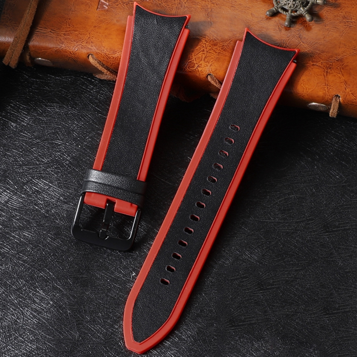 Schwarze und rote Uhrenarmbänder mit schwarzer Schnalle auf dunkler, strukturierter Oberfläche.