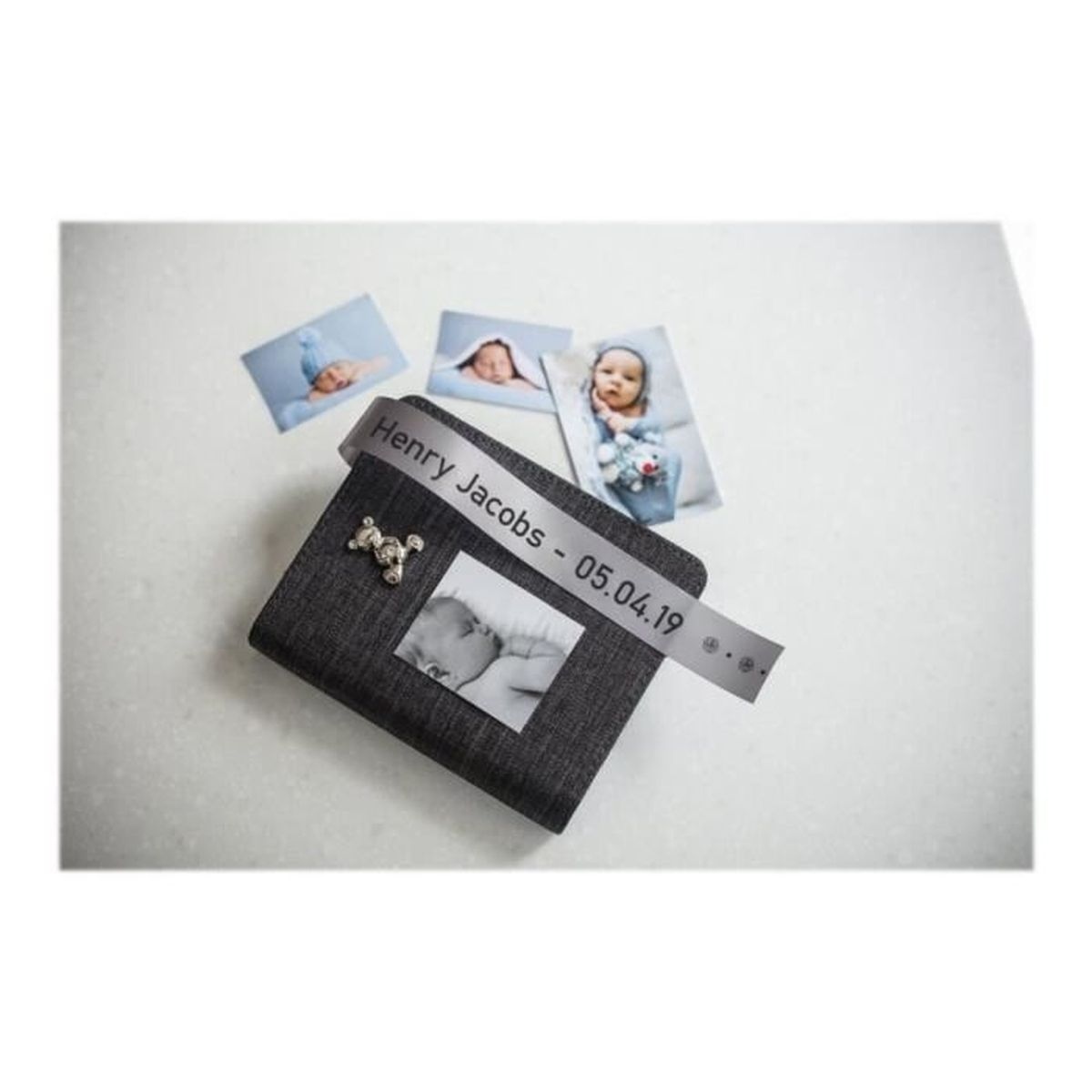 Zdjęcia i wstążka z napisem 'Henry Jacobs - 05.04.19' na szarym tle, z zawieszką misia.