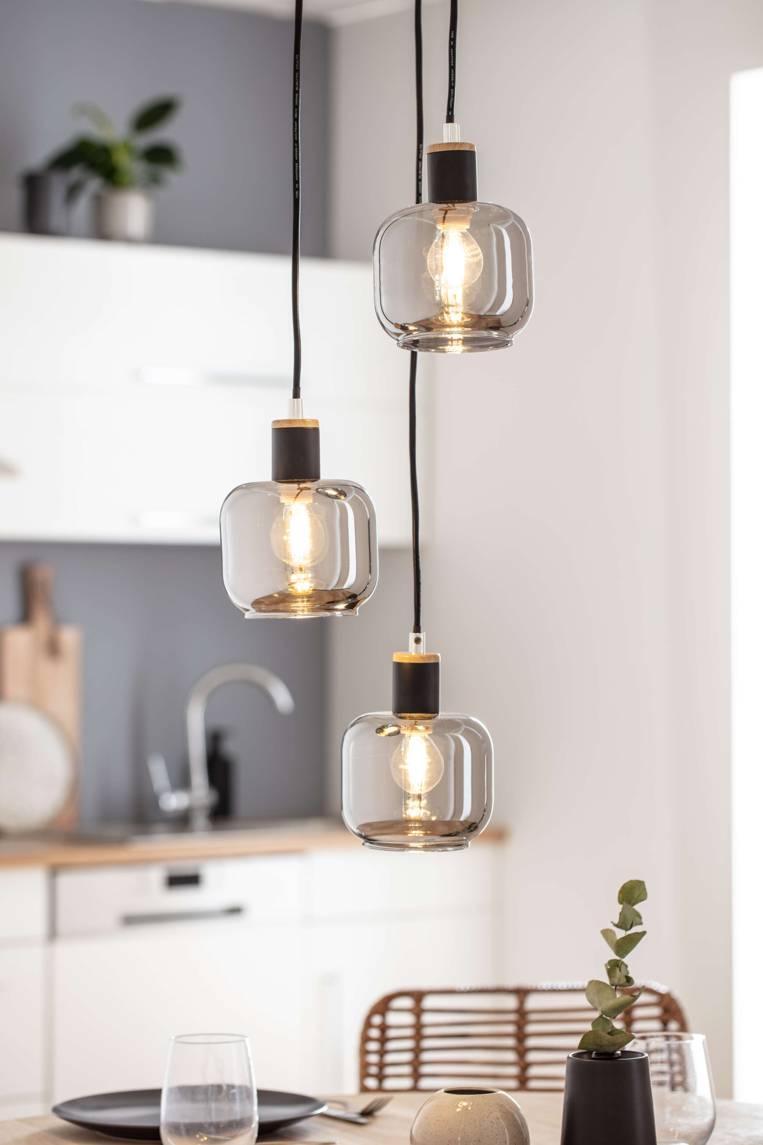 Drei Pendelleuchten mit klaren Glasschirmen und Edison-Glühbirnen, Hintergrund Küche.