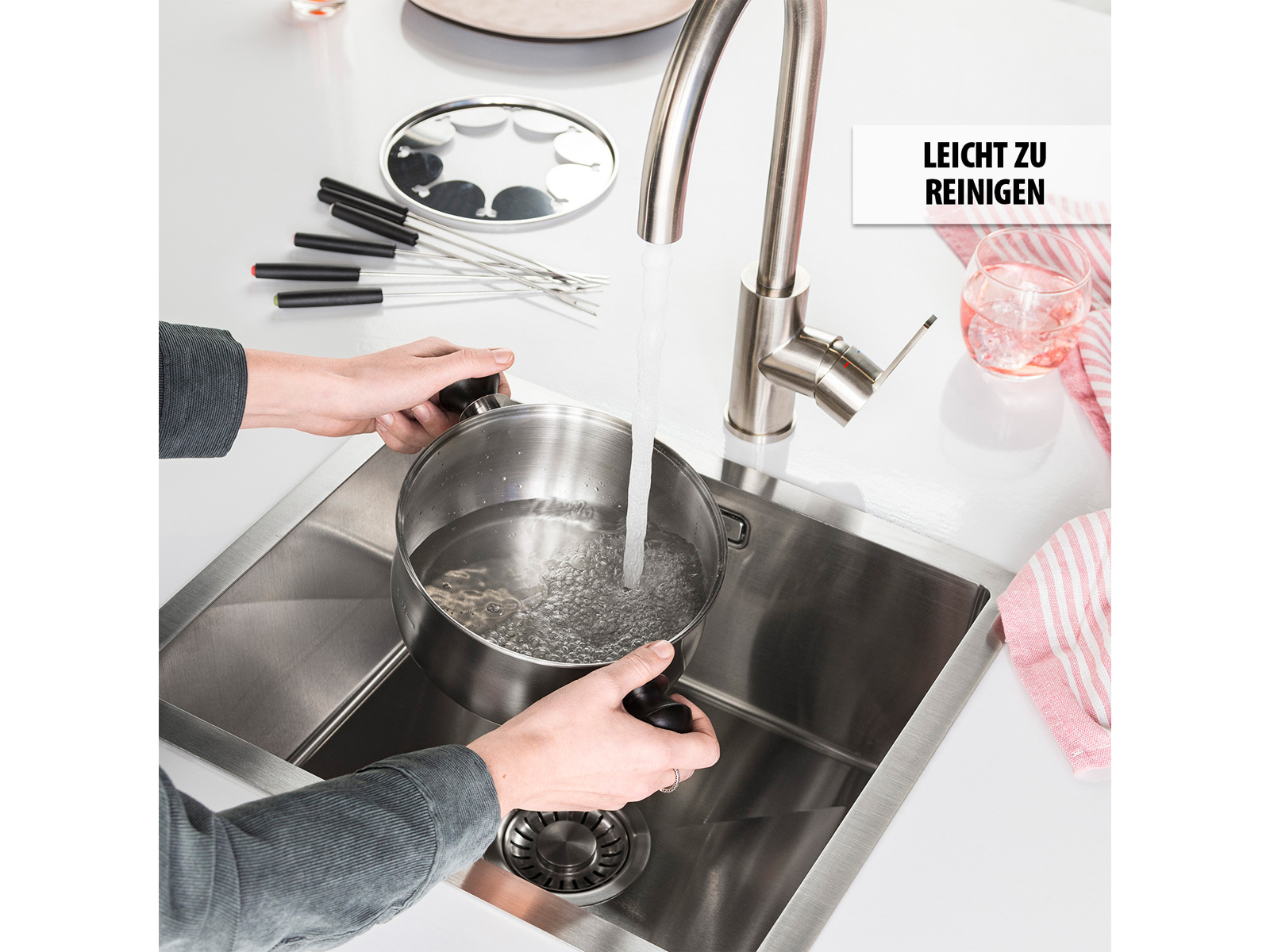 Lavello in acciaio inox con rubinetto argentato che versa acqua in una pentola. Mani che tengono la pentola.